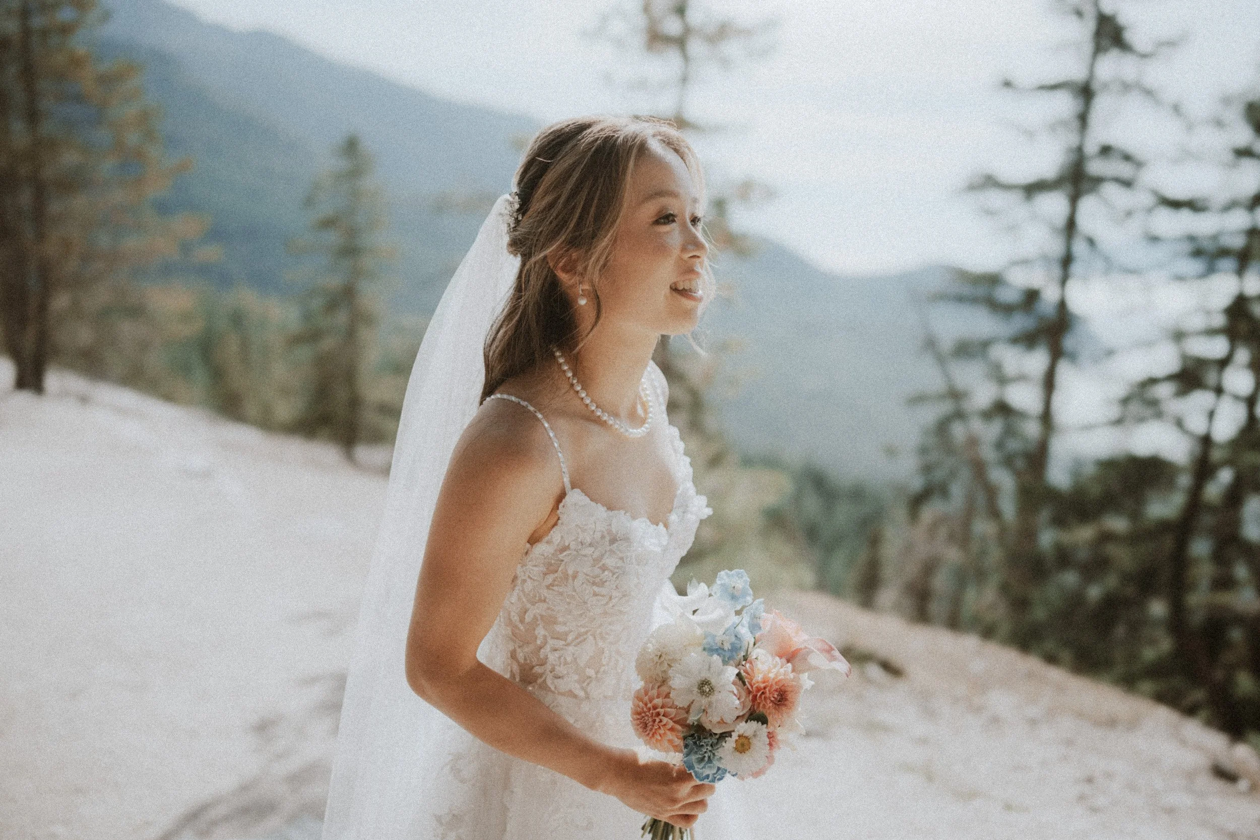 Bride holding a pink bouquet against the softly lit mountain landscape.