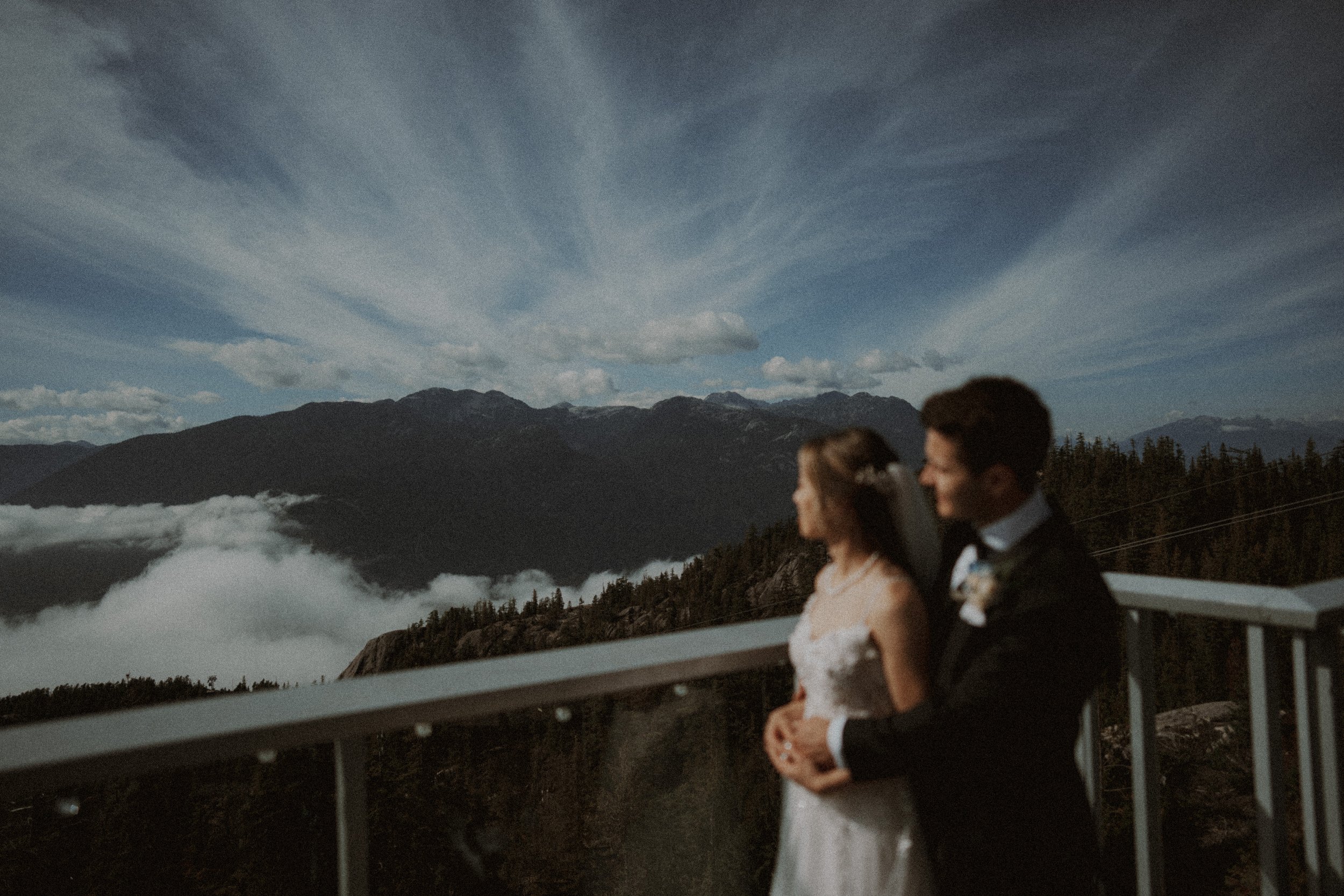 Bride and groom leaning together on a viewing deck above the cloud layer.