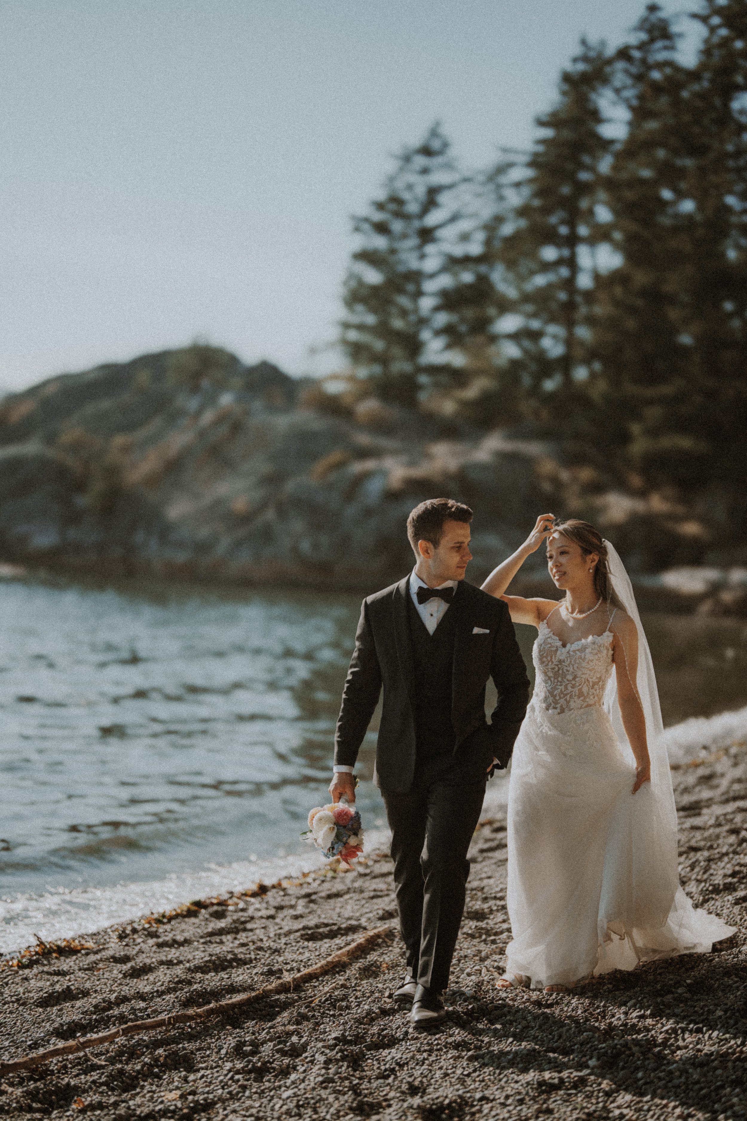 Bride and groom walking hand in hand along the pebbled shoreline.