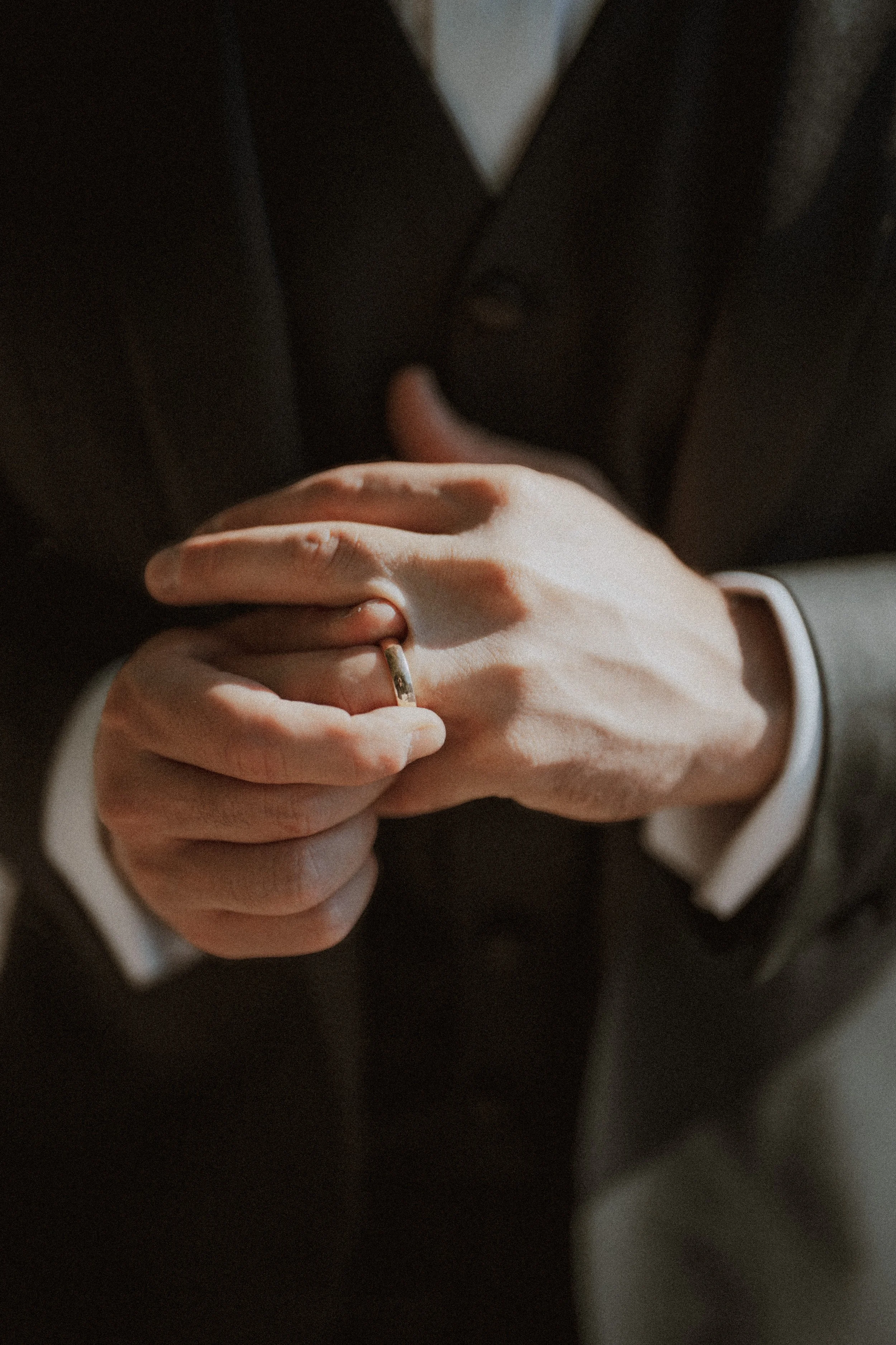 Close-up of the groom adjusting his wedding ring in sunlight.