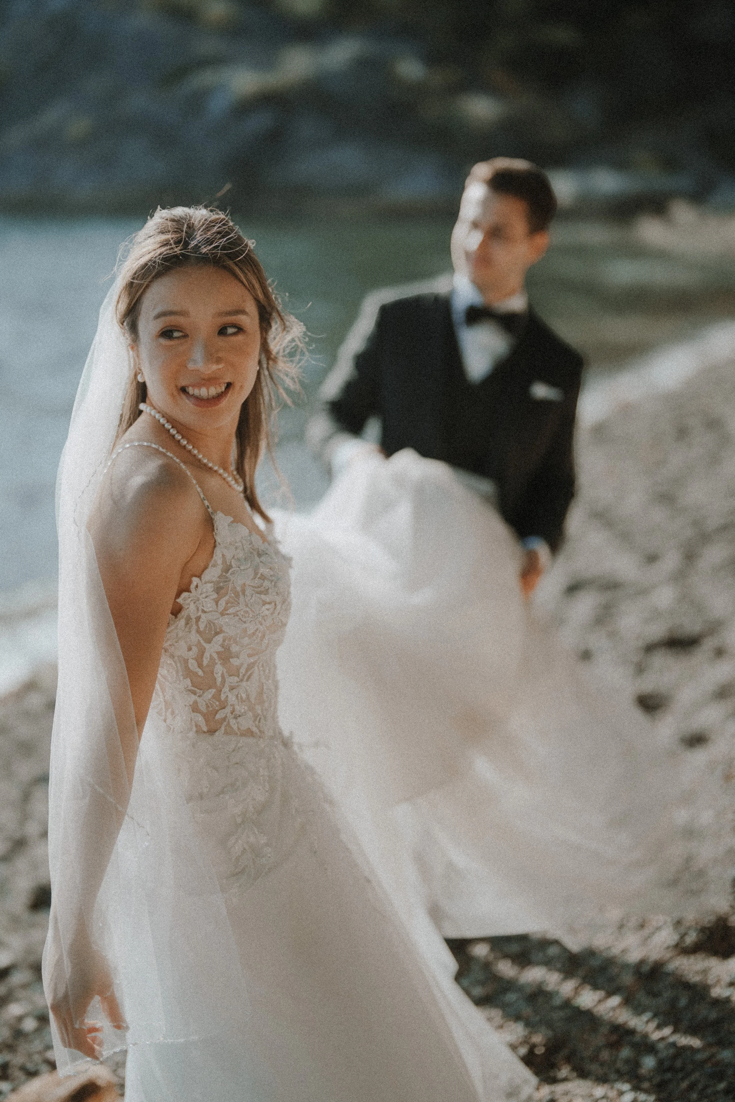 Bride looking over her shoulder as the groom holds her gown behind her.