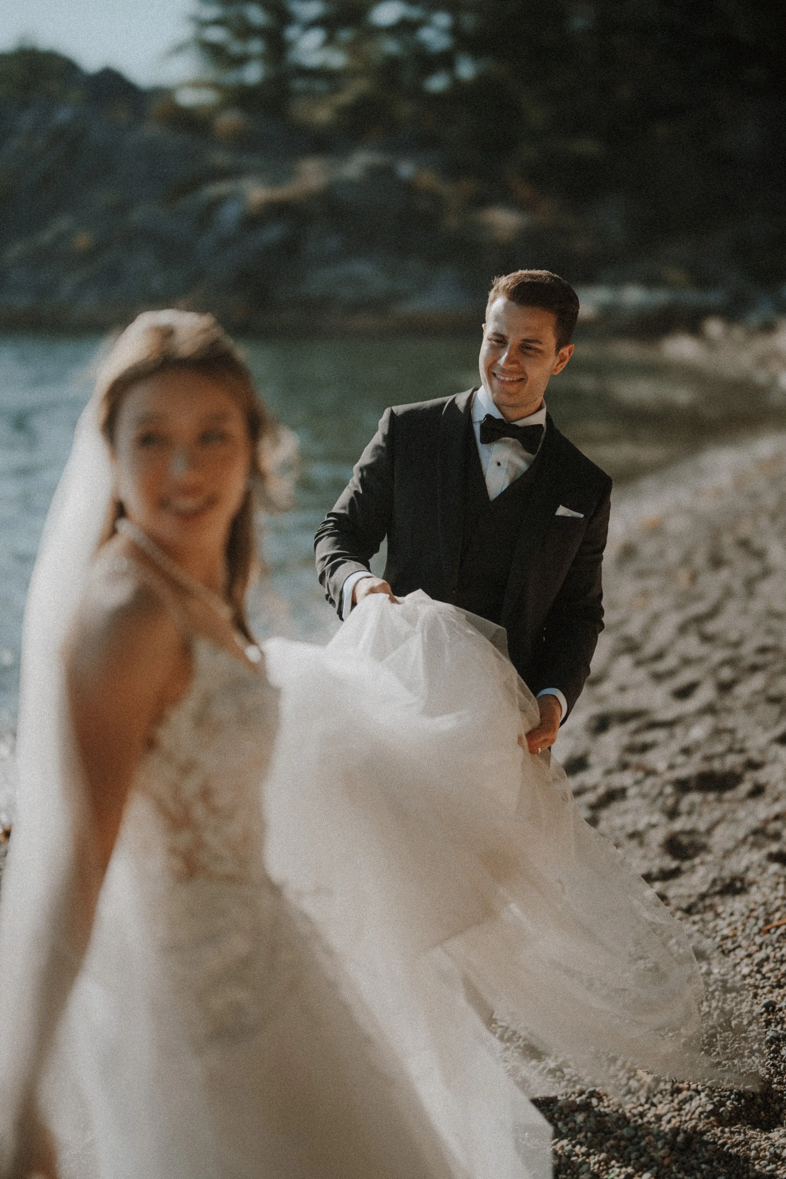 Groom helping the bride walk along the beach with her train lifted.
