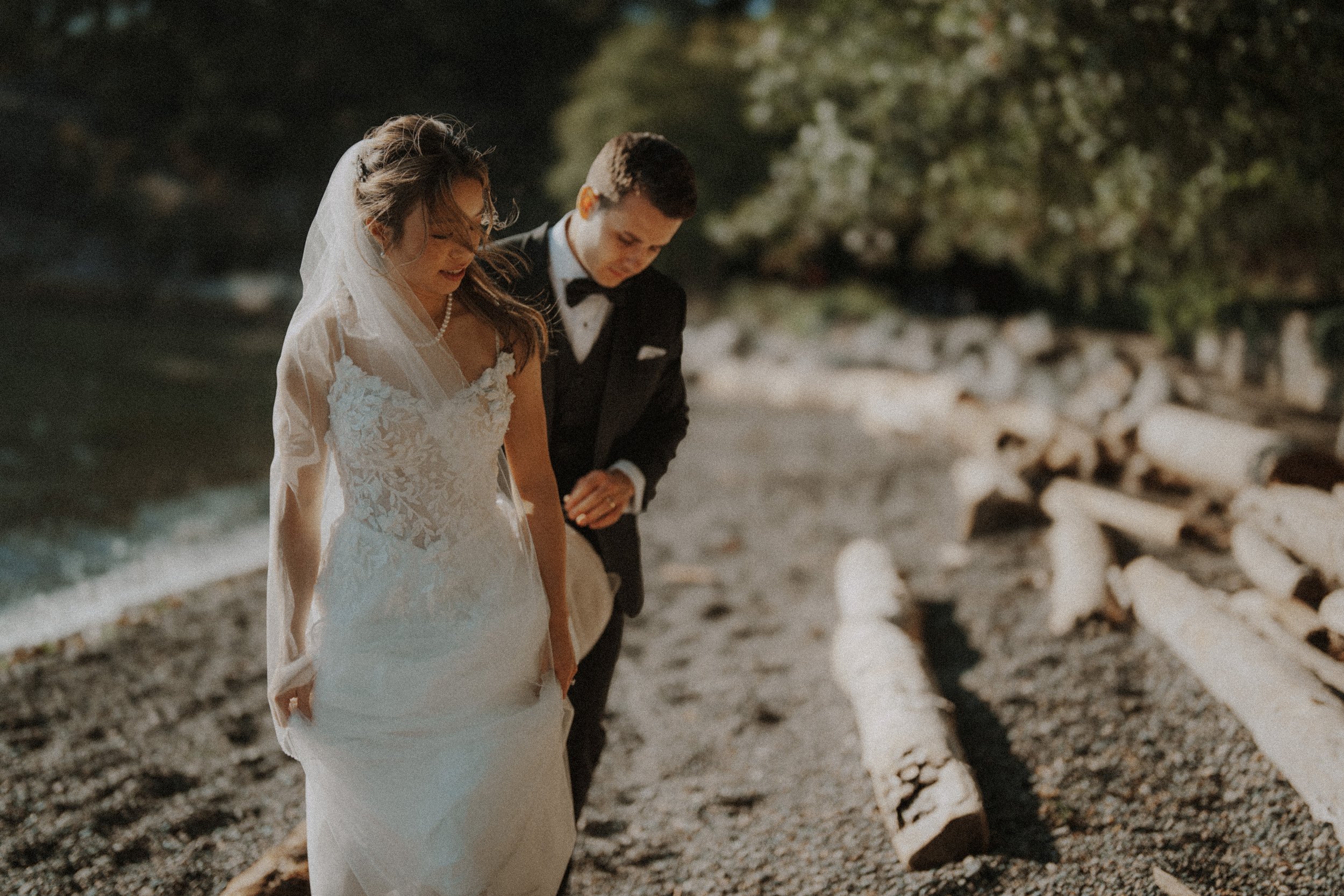 Couple walking together beside driftwood and sunlit water.