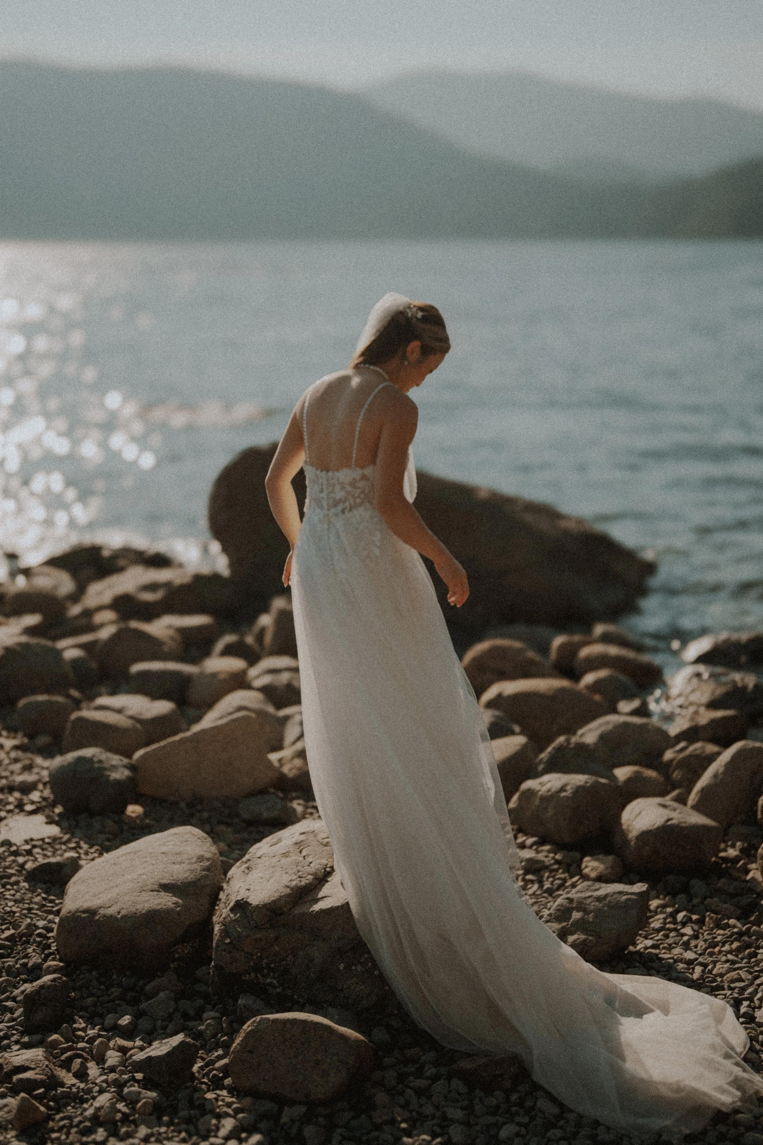 Full-length portrait of the bride standing among shoreline rocks.