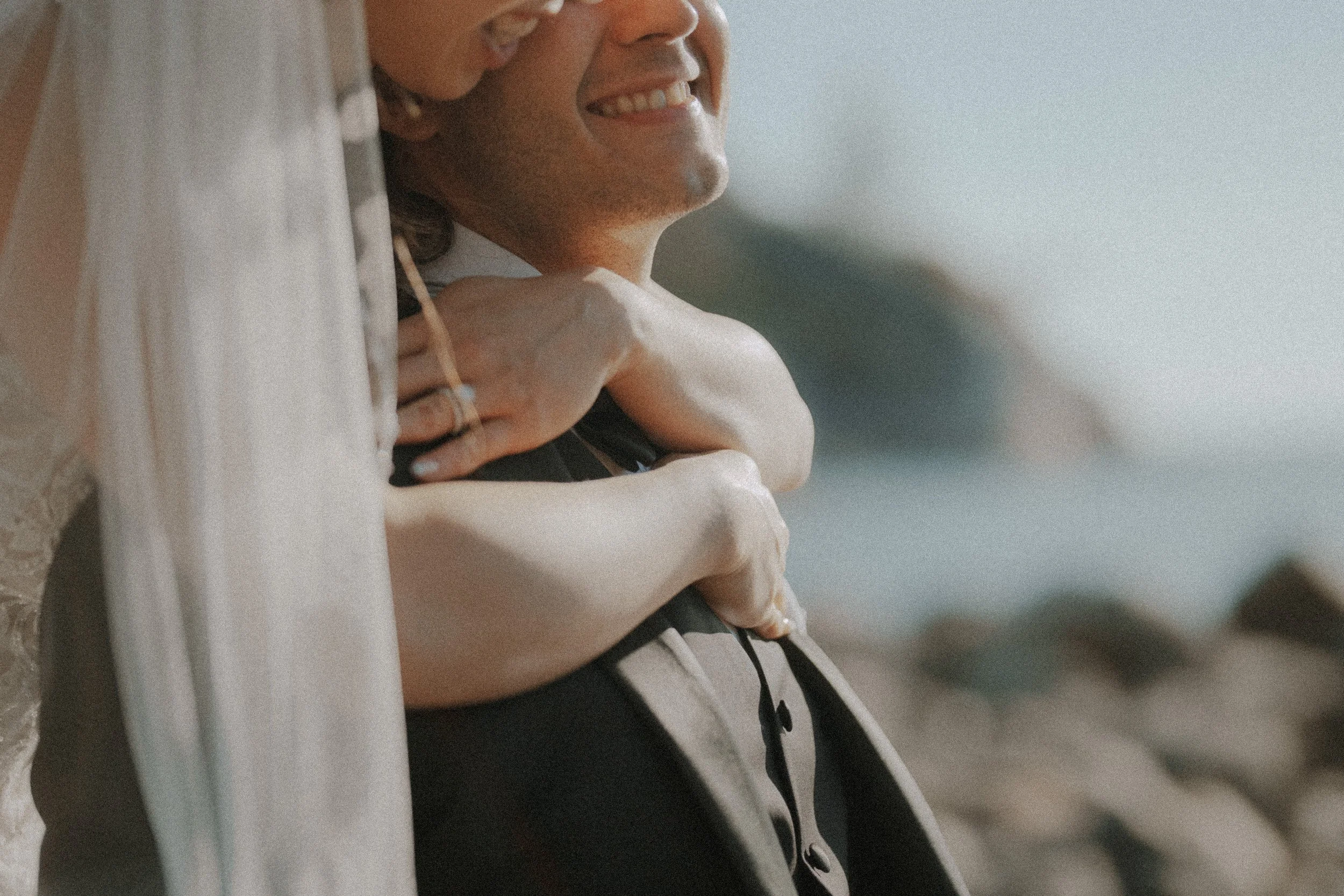 Detail of the bride's arms around the groom beneath her veil.