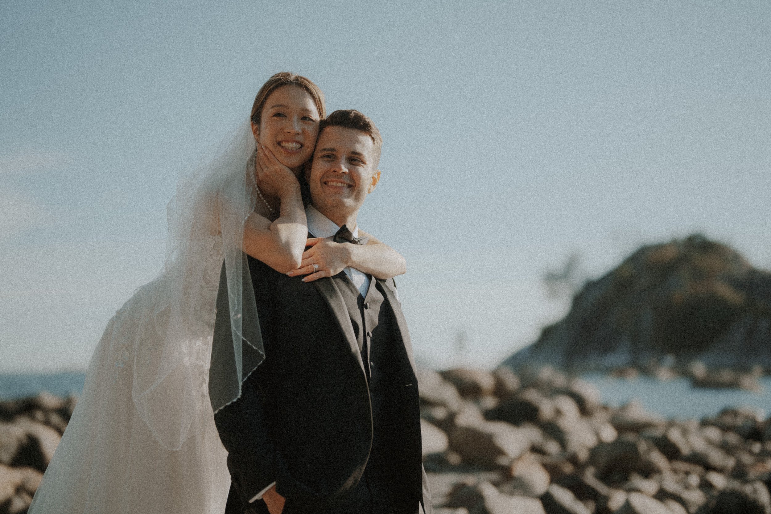 Bride and groom smiling together on the rocky Whytecliff Park shoreline.