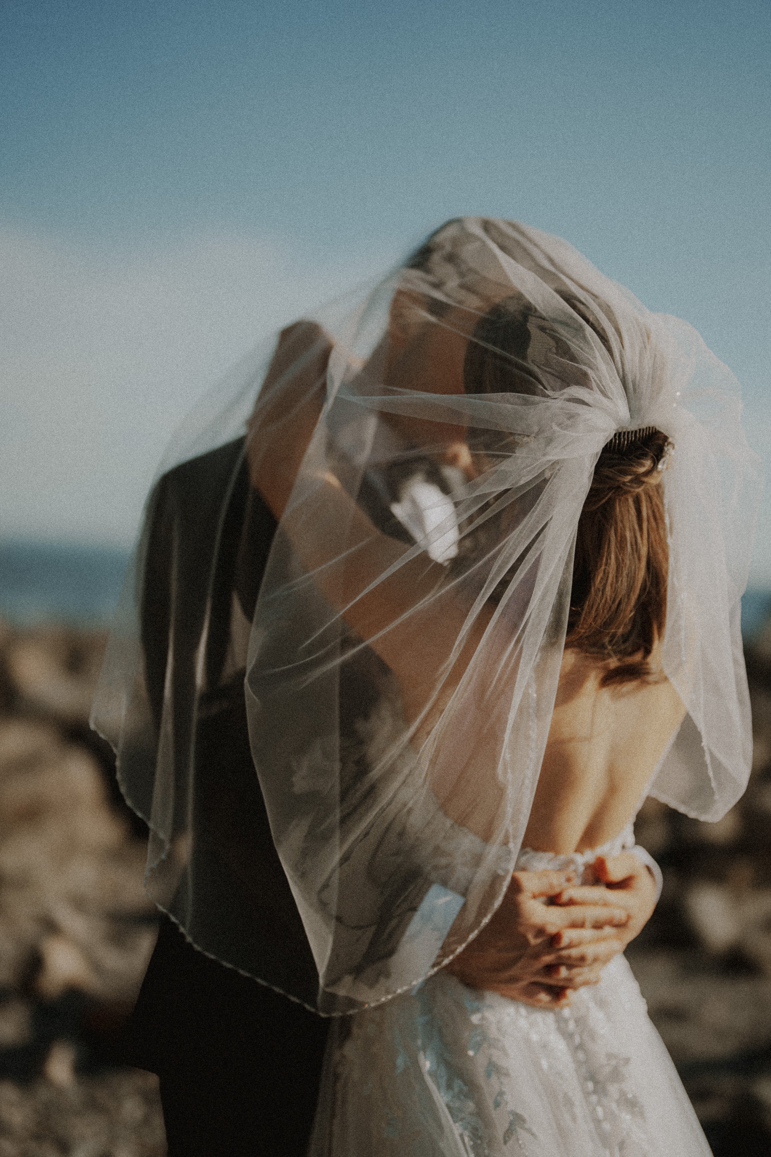 Couple embracing beneath a veil blowing in the sea breeze.