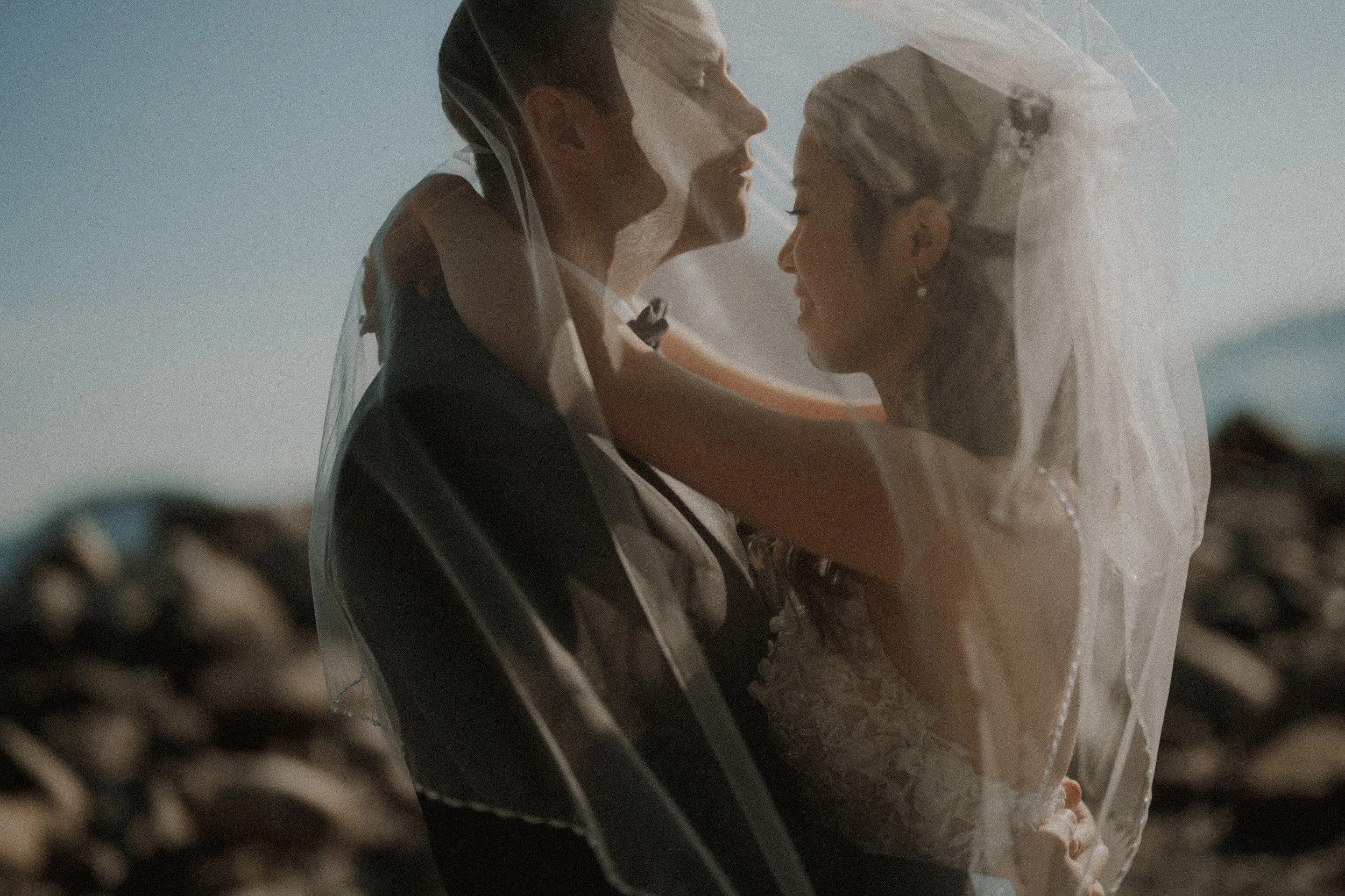 Bride touching the groom's face through her softly lit veil.