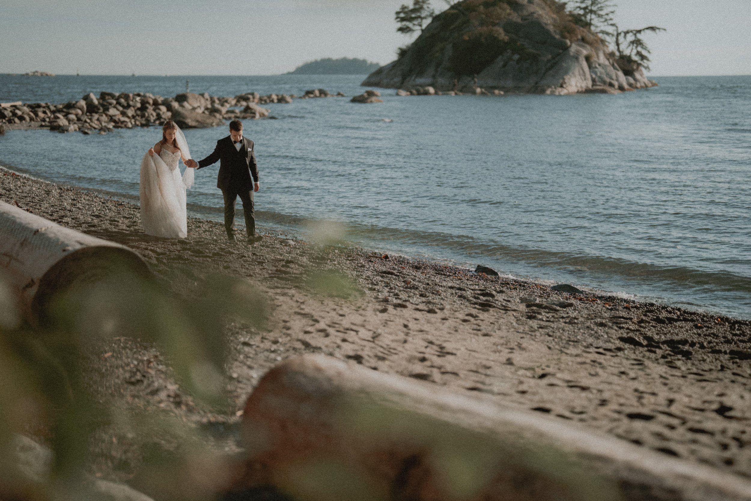 Wide view of newlyweds walking along the shore near Whytecliff Park's rocky island.