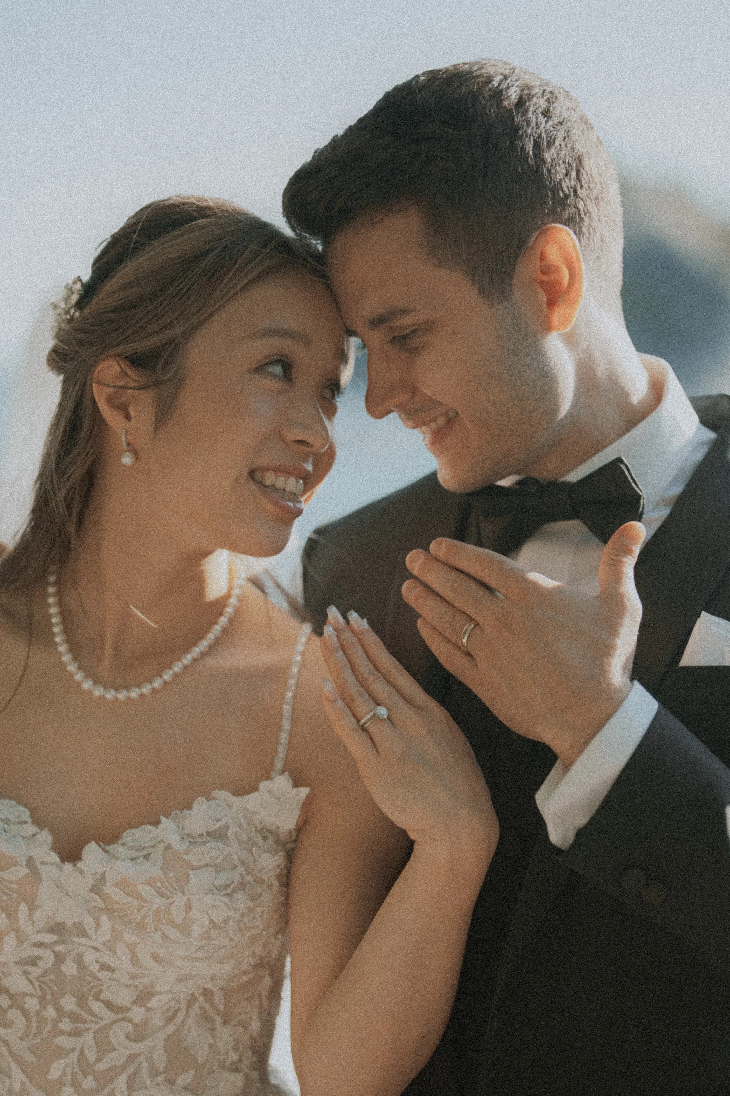 Newlyweds smiling and touching foreheads beside the coast.