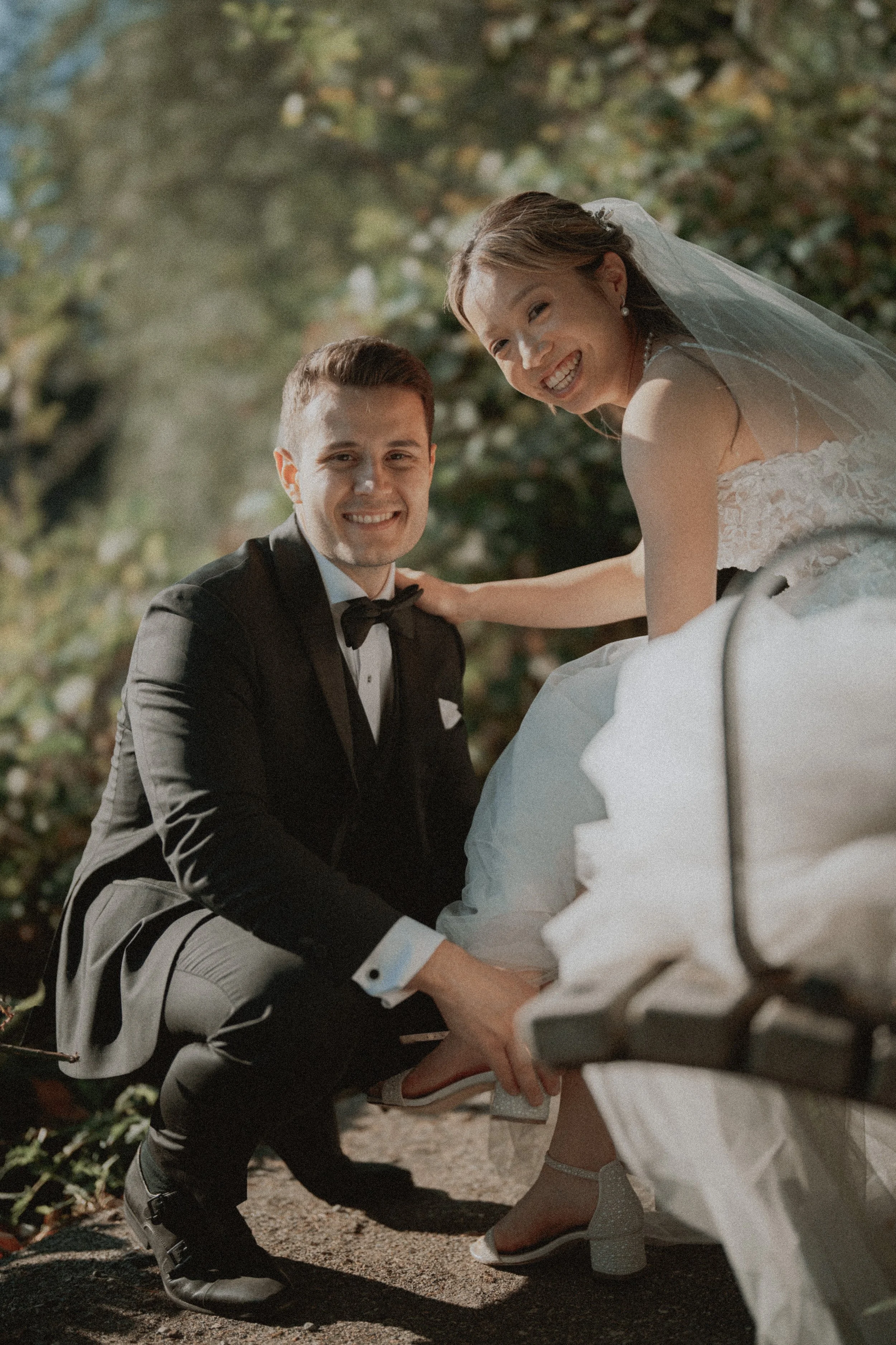 Couple smiling together beside a wooden bench on the pebbled beach.