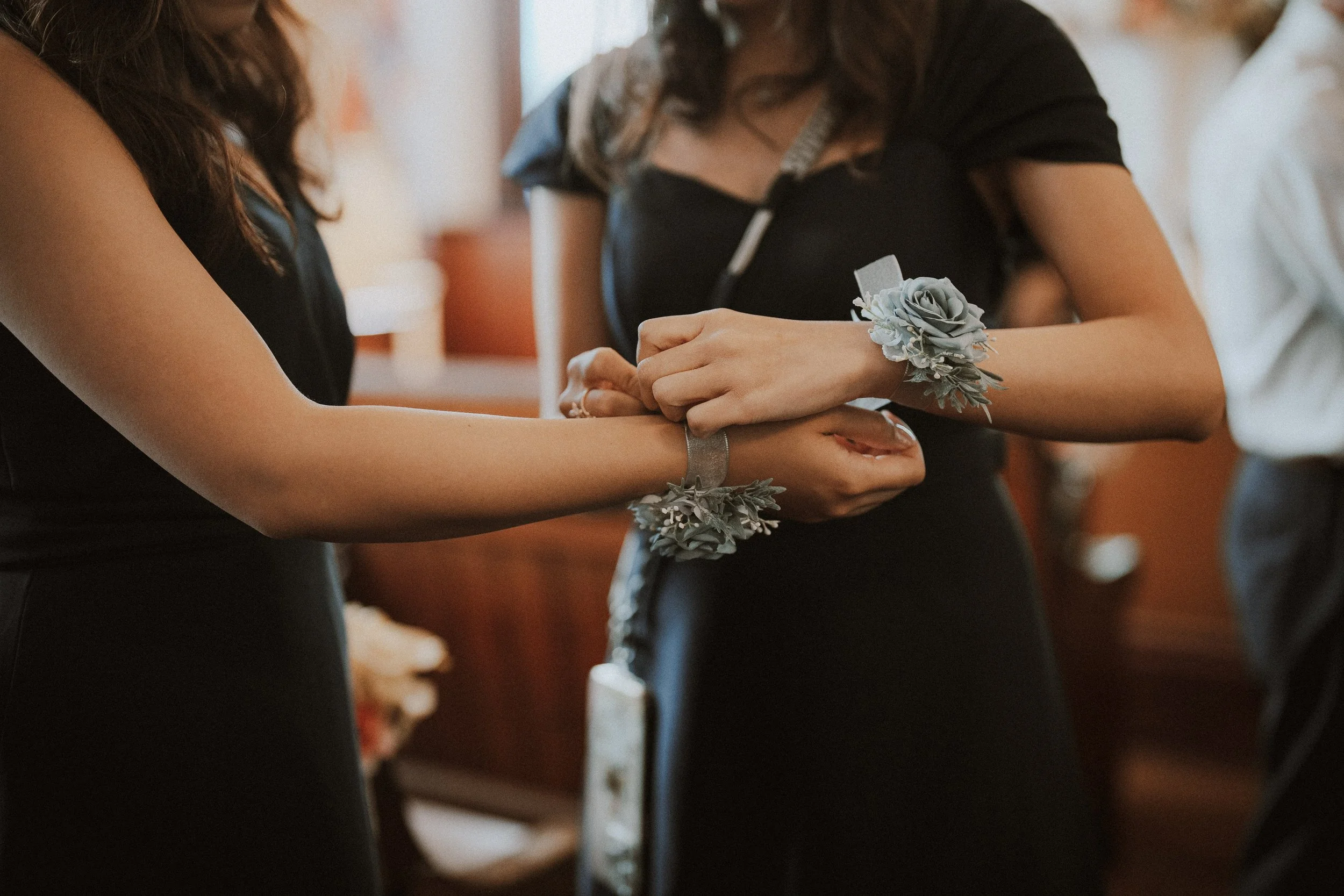 Bridesmaid helping fasten a floral wrist corsage before the ceremony.