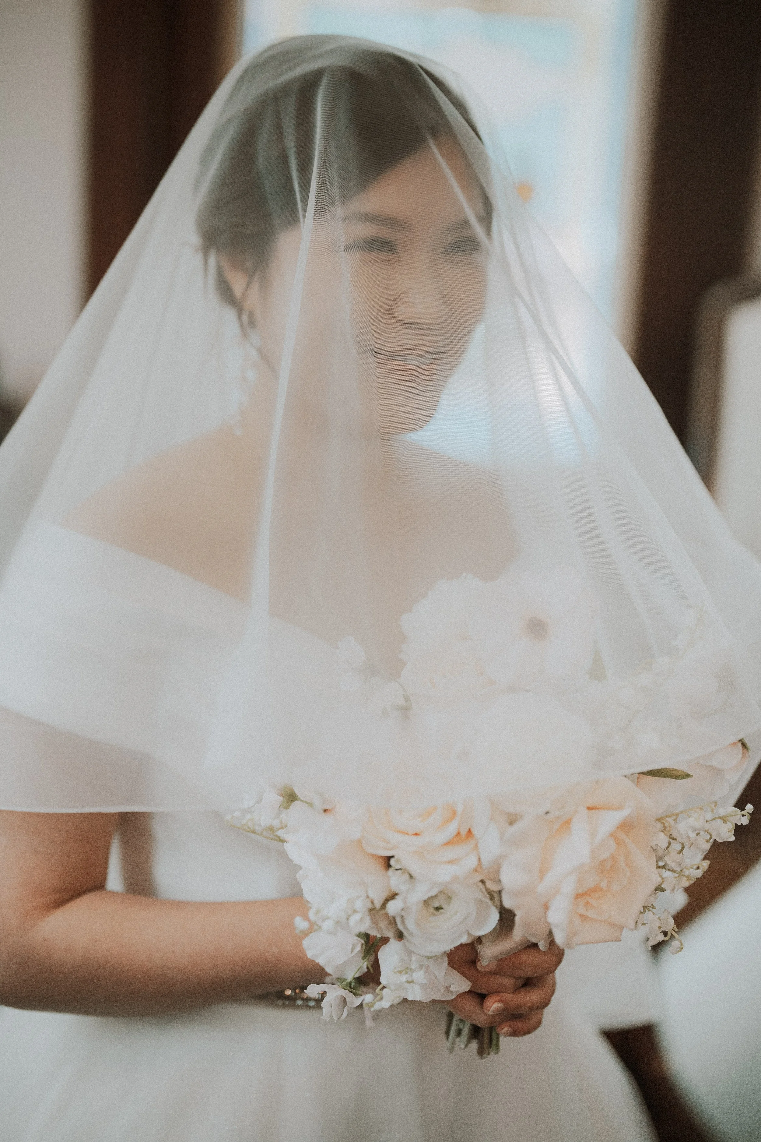 Portrait of the bride holding a pale bouquet beneath her wedding veil.