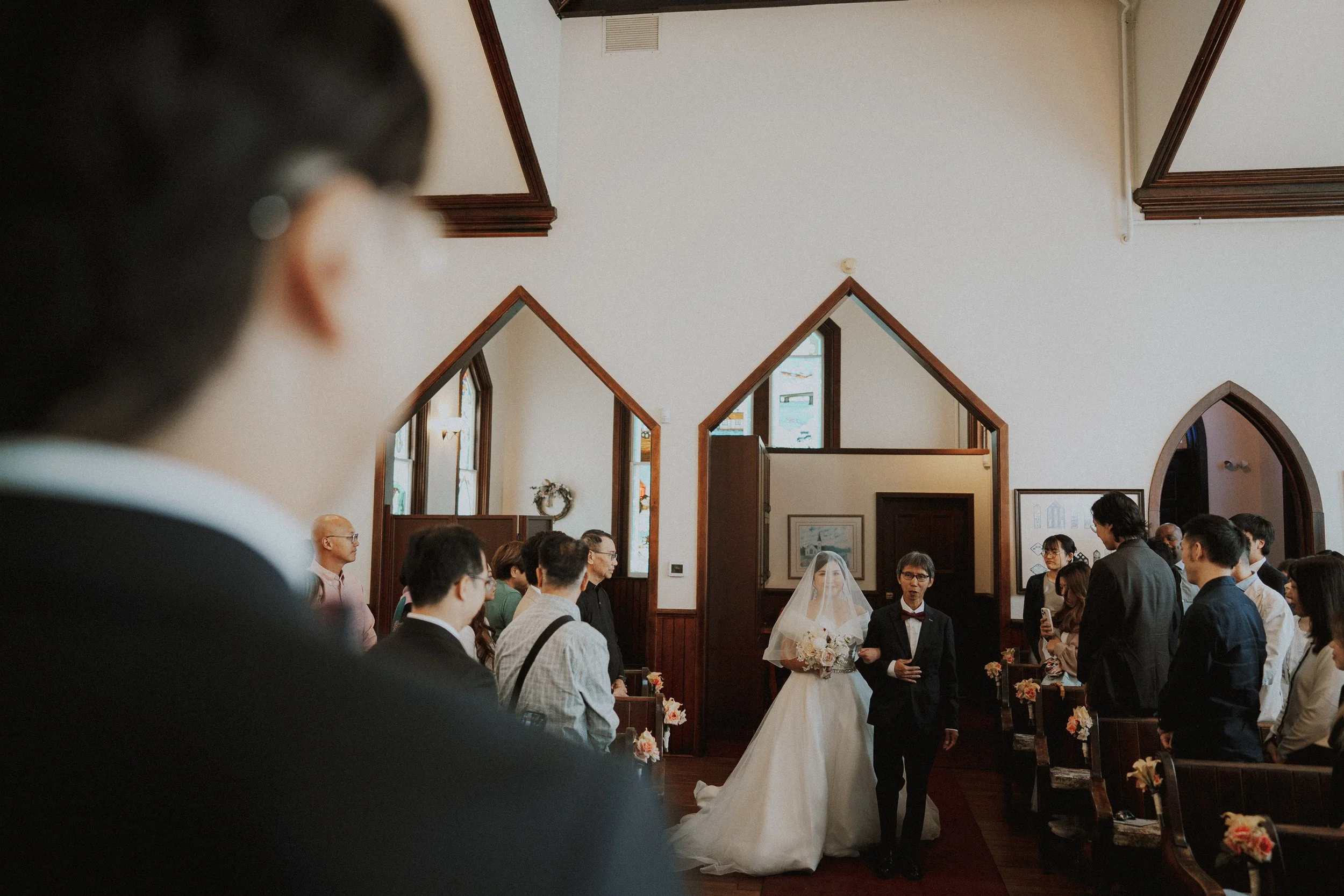 View past the groom toward the bride entering the chapel aisle.