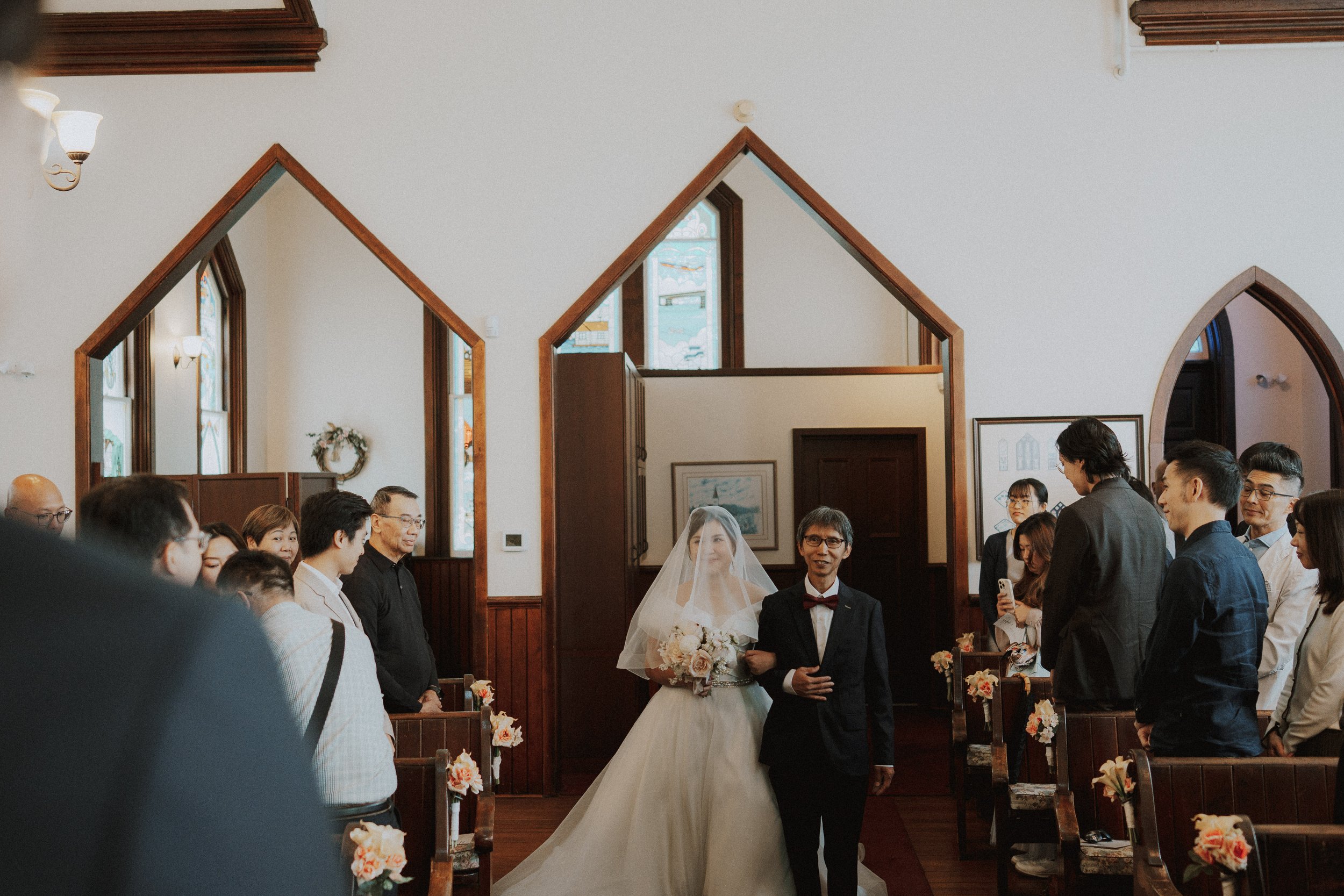 Bride approaching the front of Minoru Chapel while guests stand beside the pews.