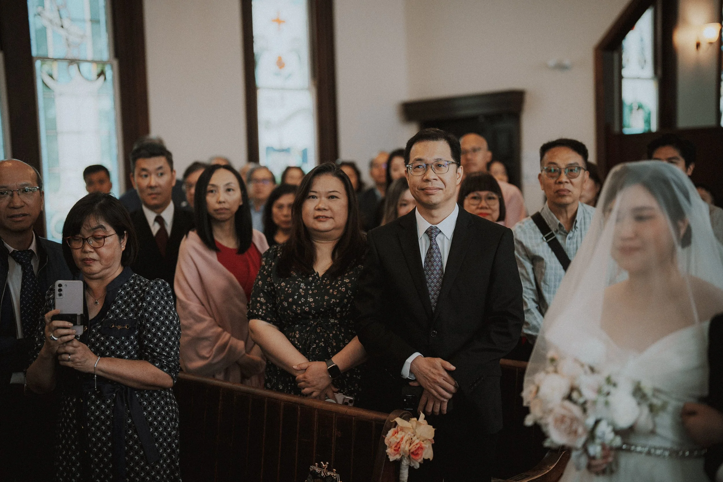 Standing wedding guests watching the bride pass through the chapel.