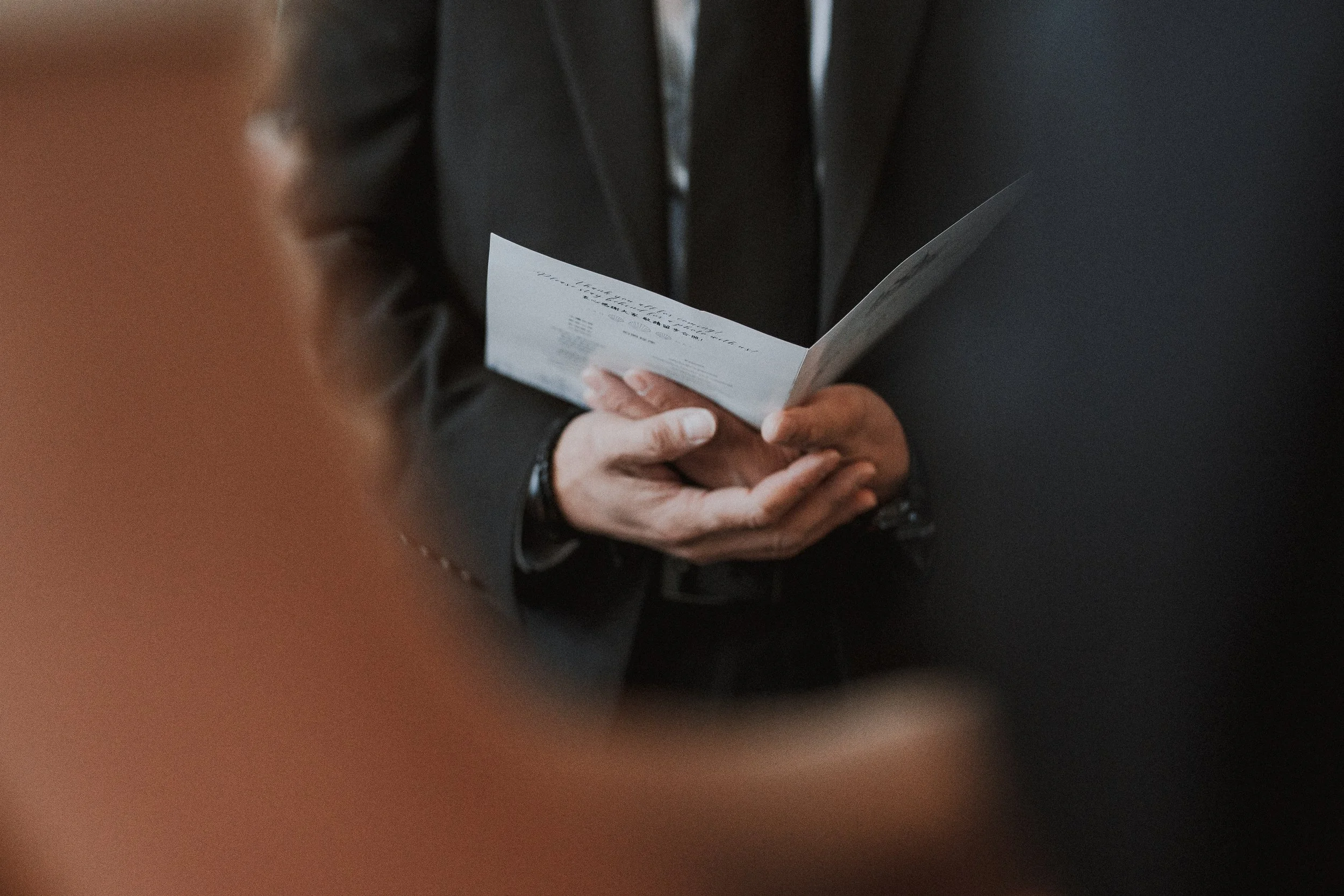 Close-up of the groom's hands holding a folded wedding ceremony card.