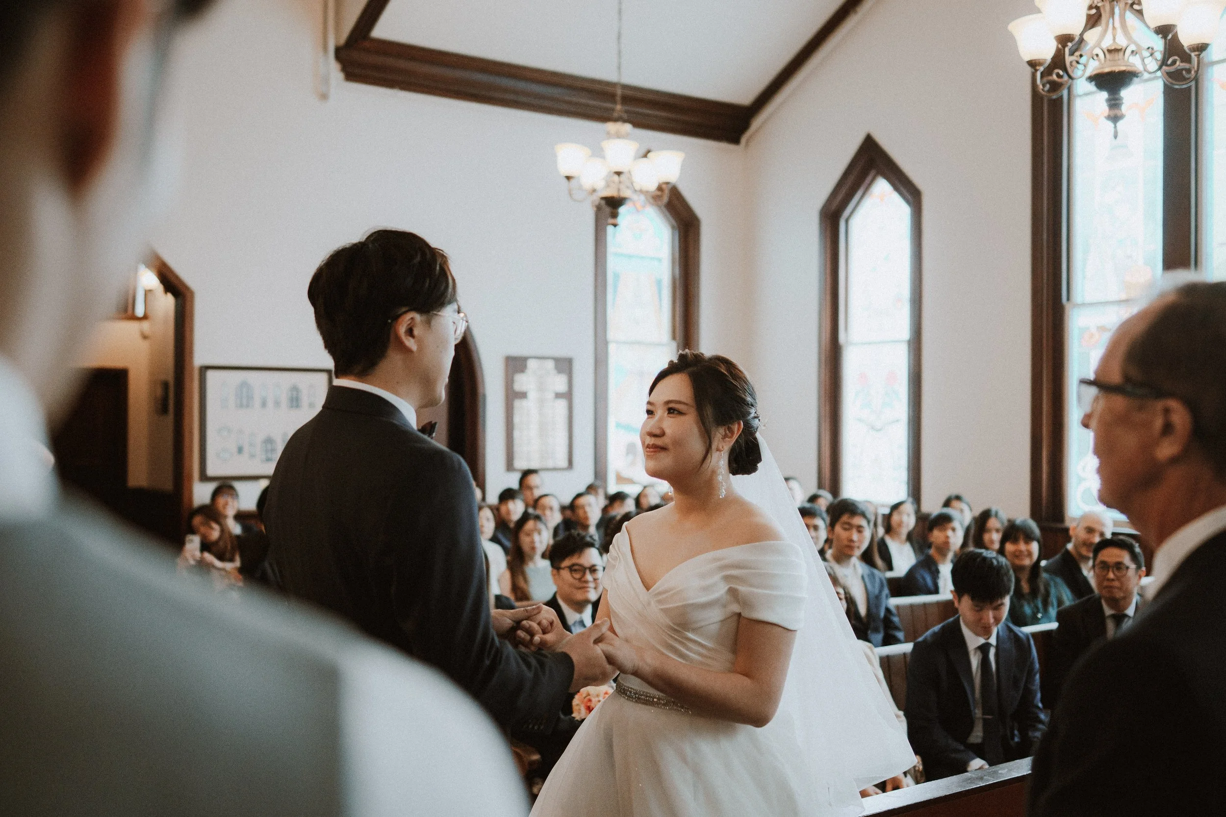 Bride speaking to the groom while guests listen from the chapel pews.