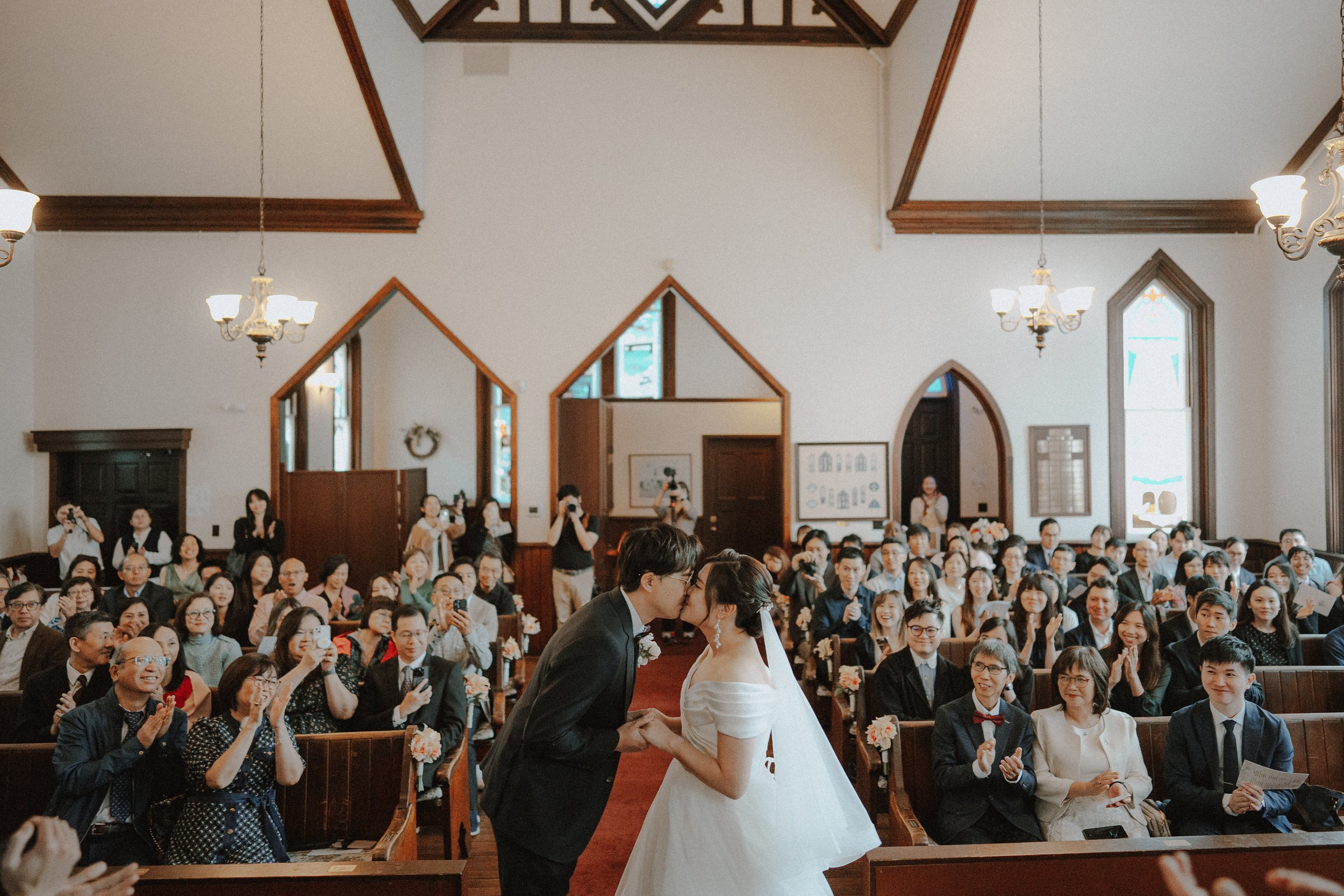 Couple sharing their first kiss as guests applaud inside Minoru Chapel.