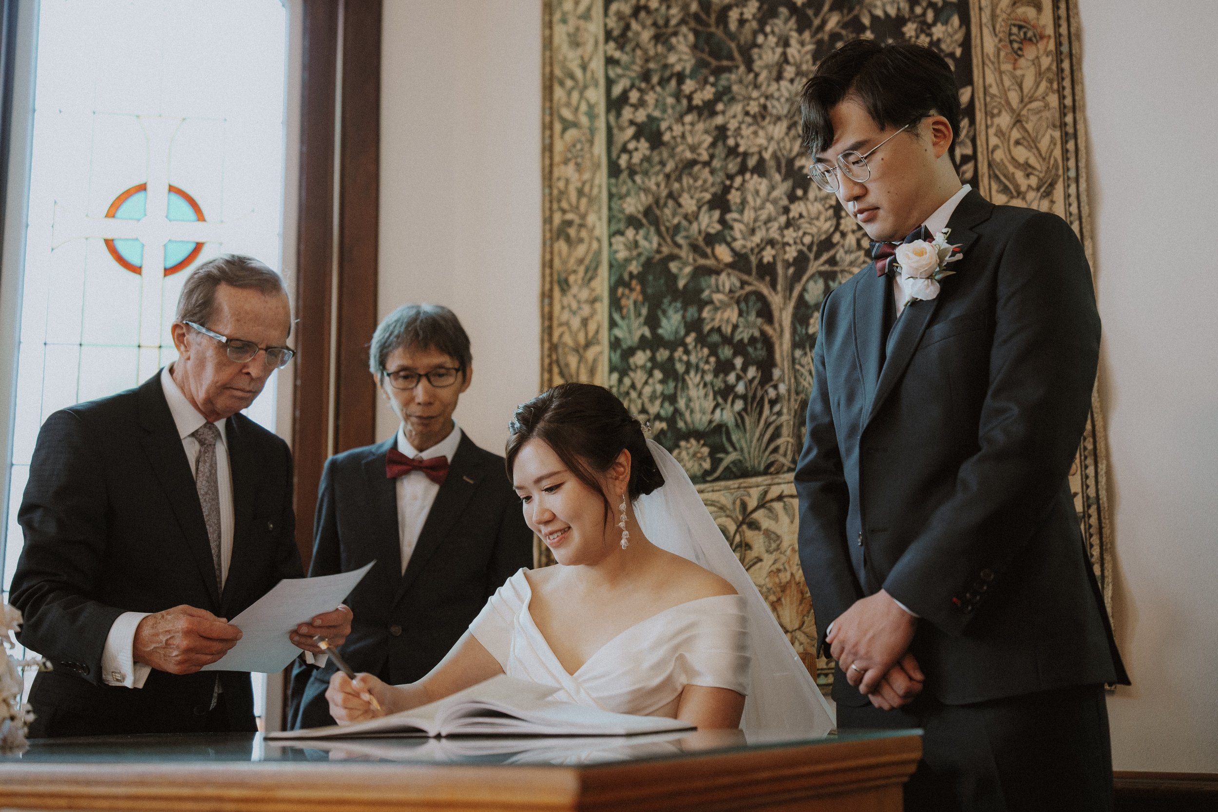Bride signing wedding documents with the groom and witnesses beside her.