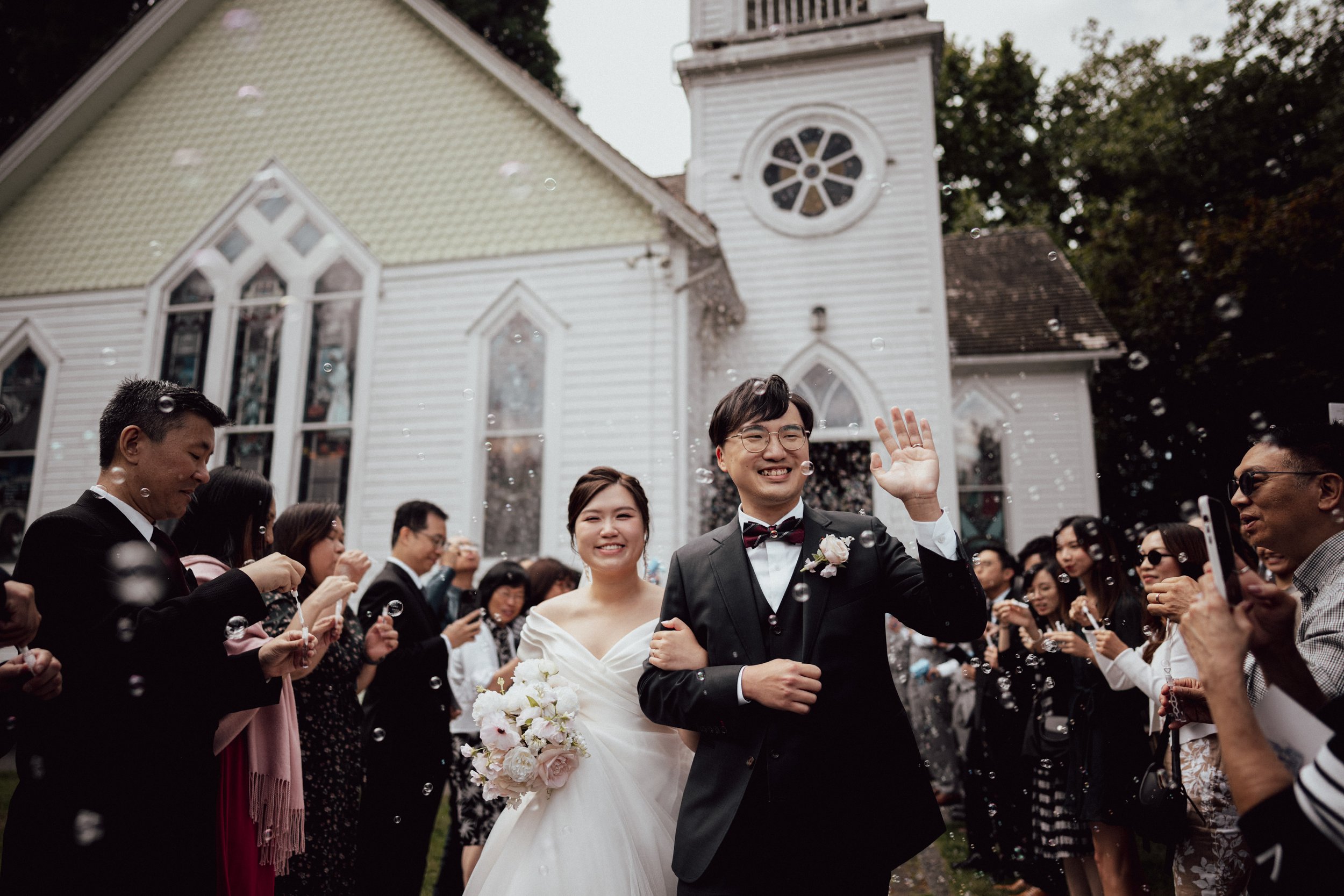 Bride and groom waving as they leave the chapel through celebrating guests.