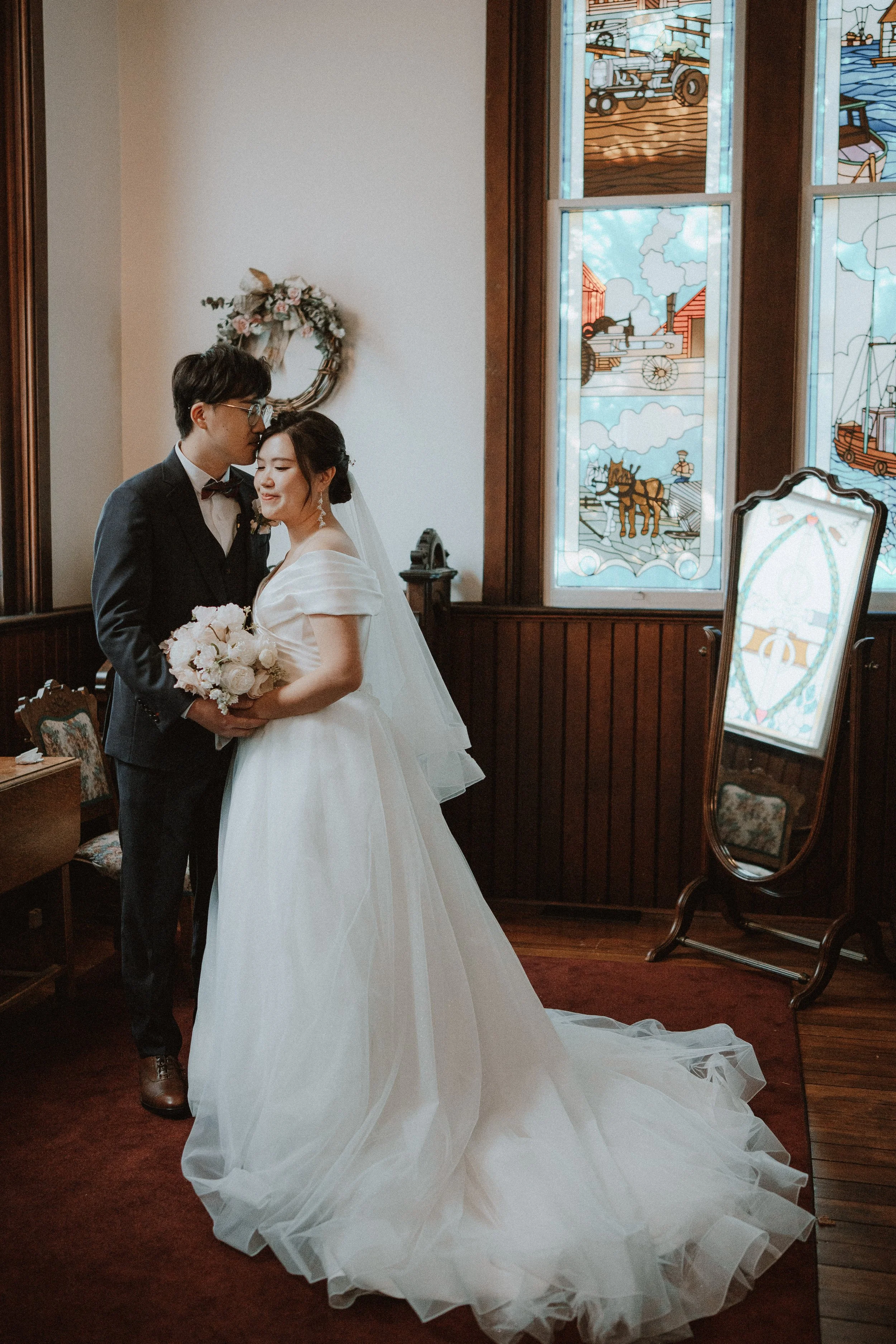 Bride and groom embracing beside Minoru Chapel's stained-glass windows.