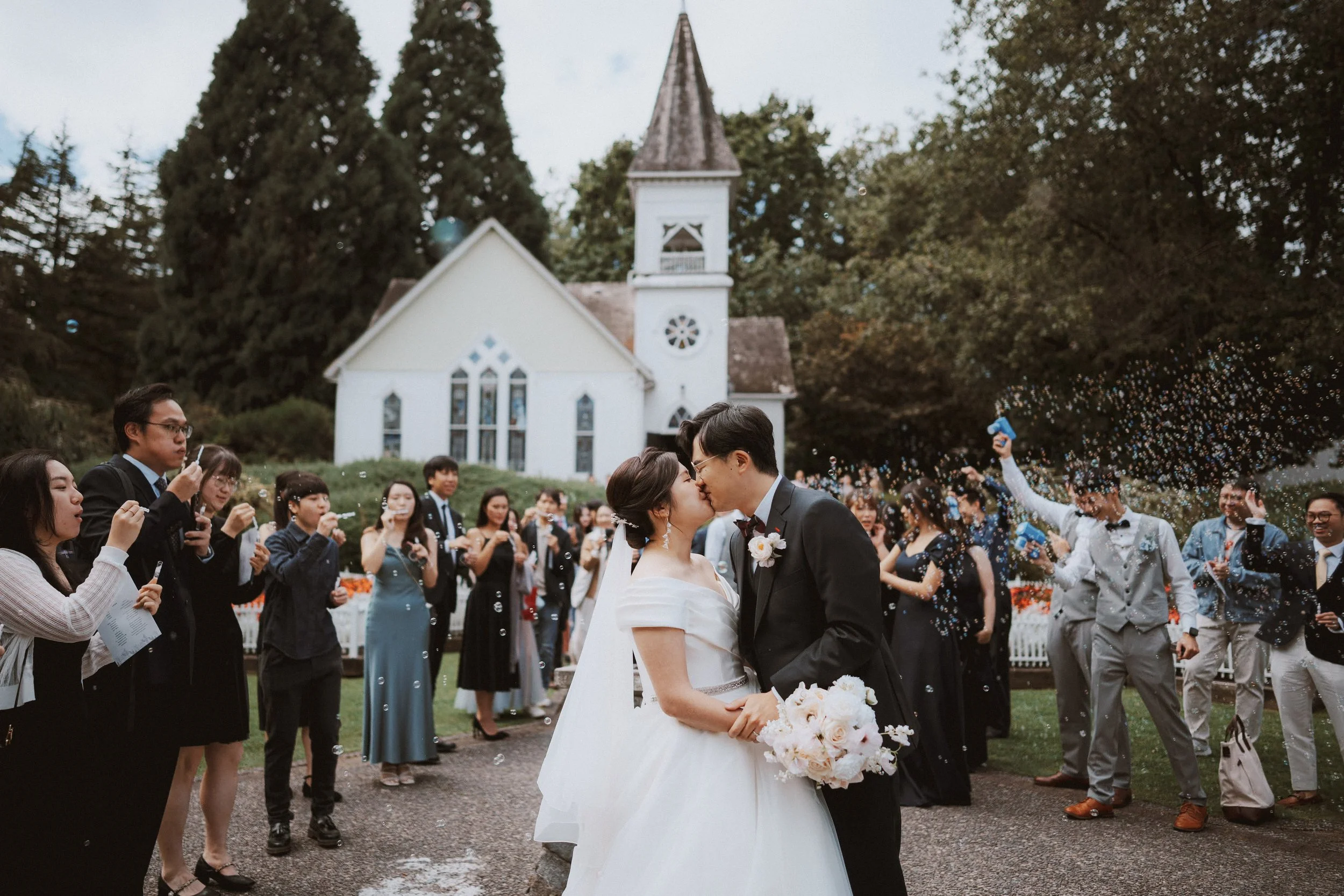 Couple kissing on the path outside Minoru Chapel as guests celebrate.