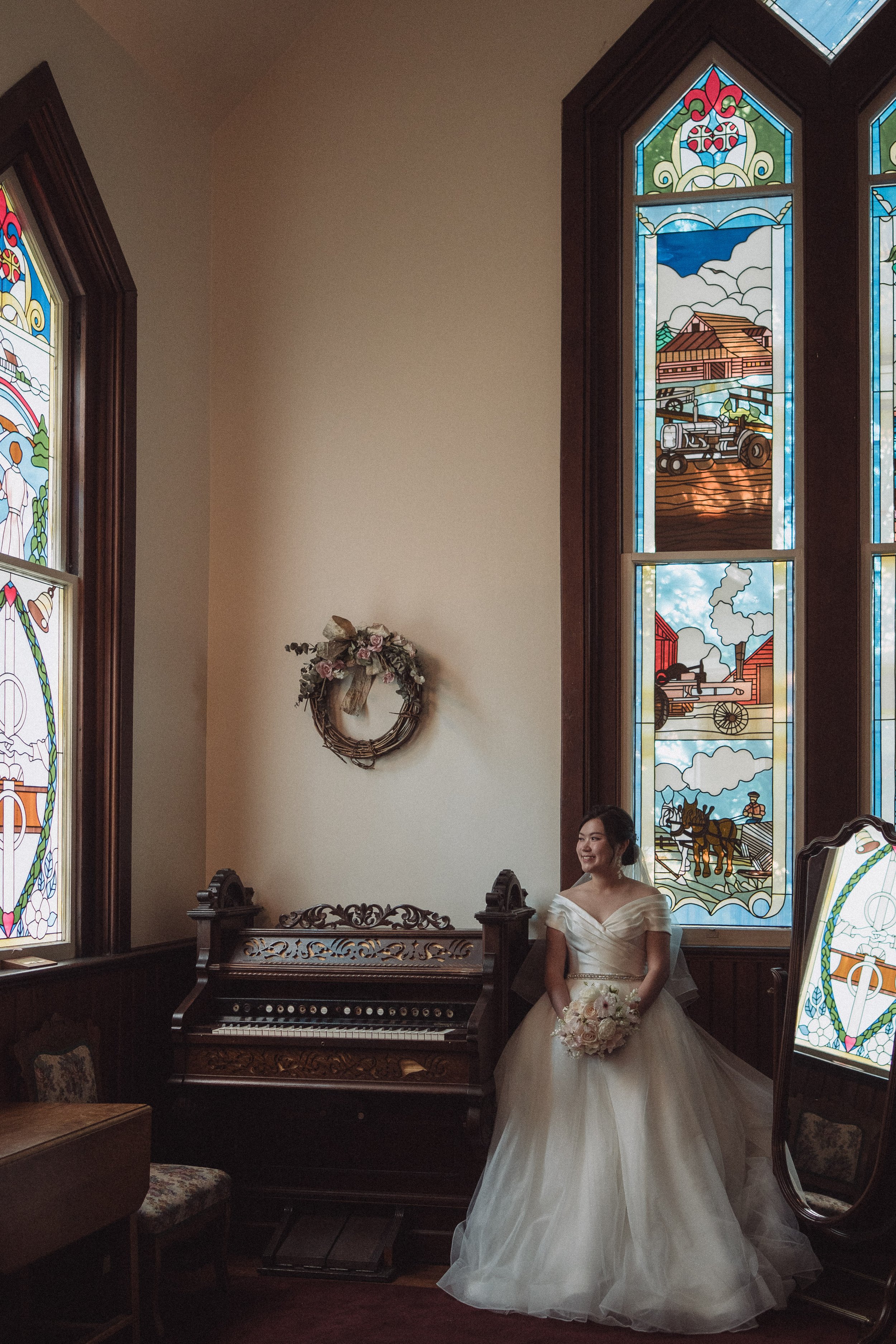 Bride standing beside tall stained-glass windows with her bouquet.