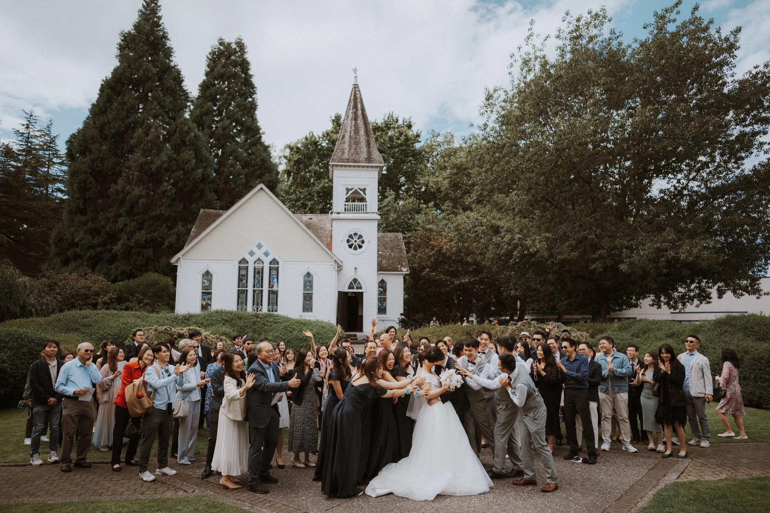 Wedding guests celebrating around the couple on the chapel garden path.