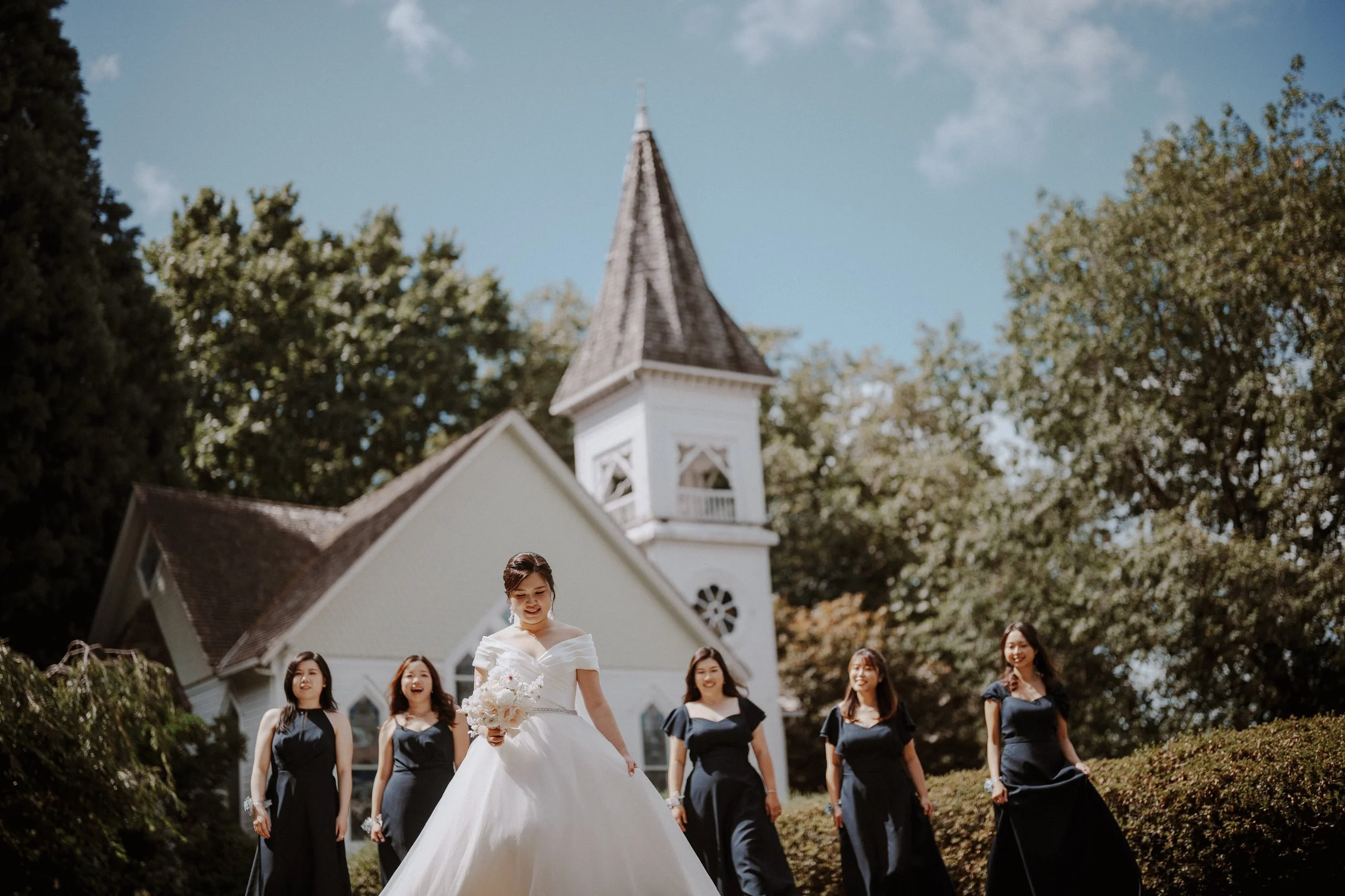 Bride stepping forward with her bridesmaids on the Minoru Chapel lawn.