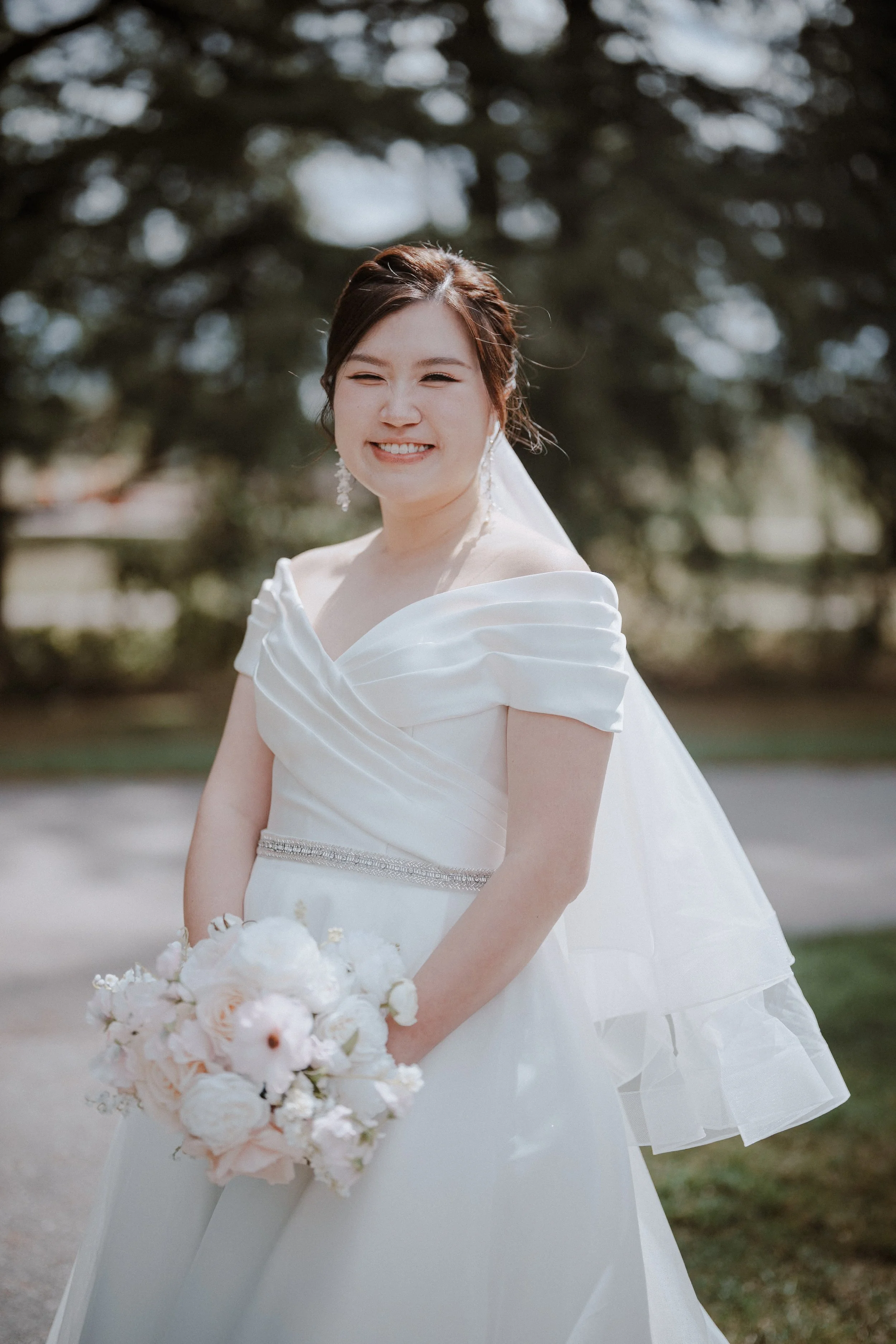 Outdoor portrait of the bride in an off-the-shoulder gown and veil.