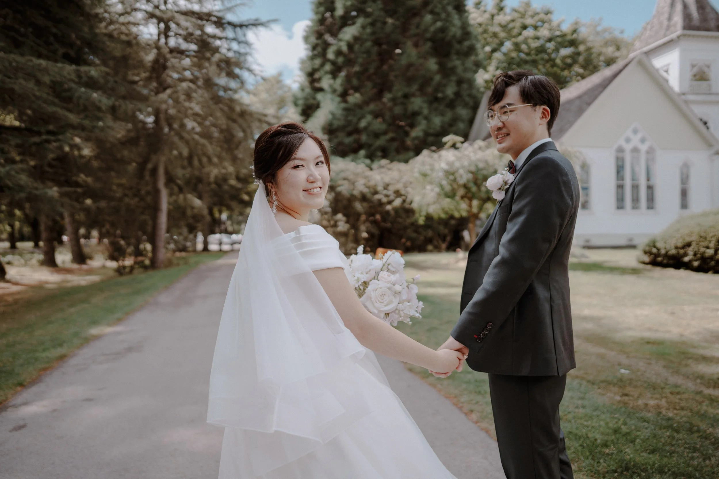 Bride and groom looking back while holding hands on a garden path.