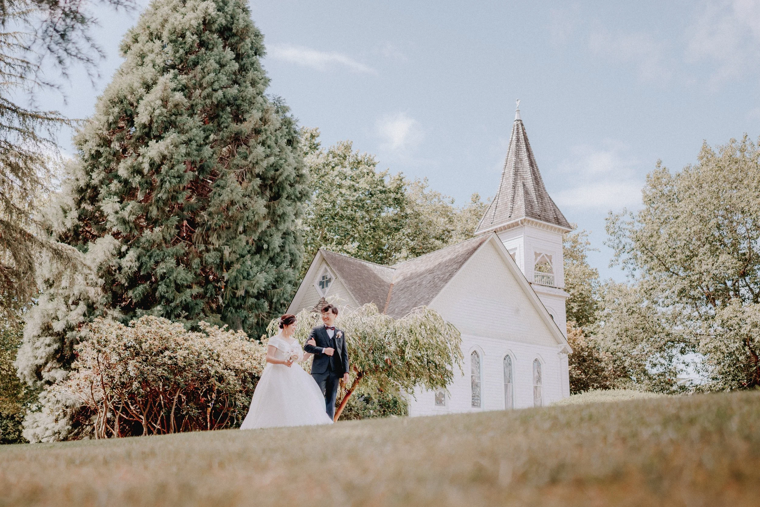 Wide portrait of the newlyweds beside Minoru Chapel and its garden trees.
