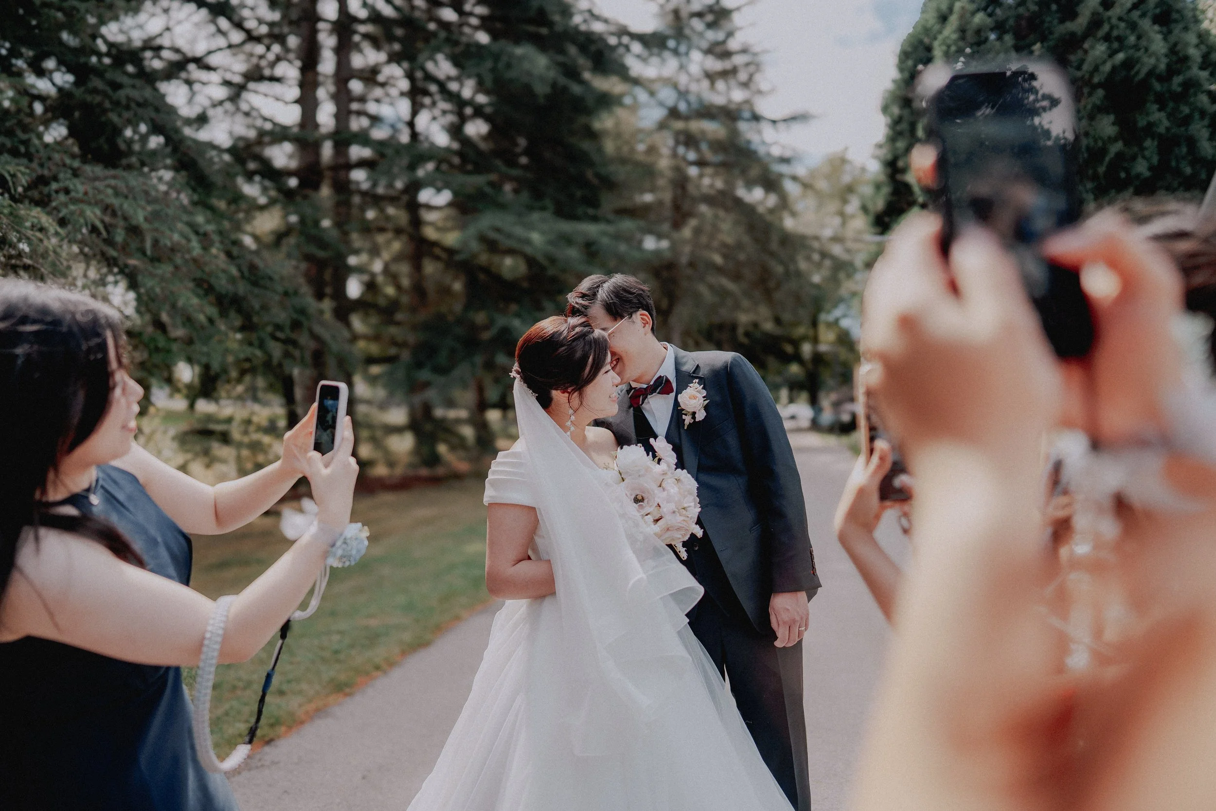 Guests photographing the couple sharing a kiss on the garden path.