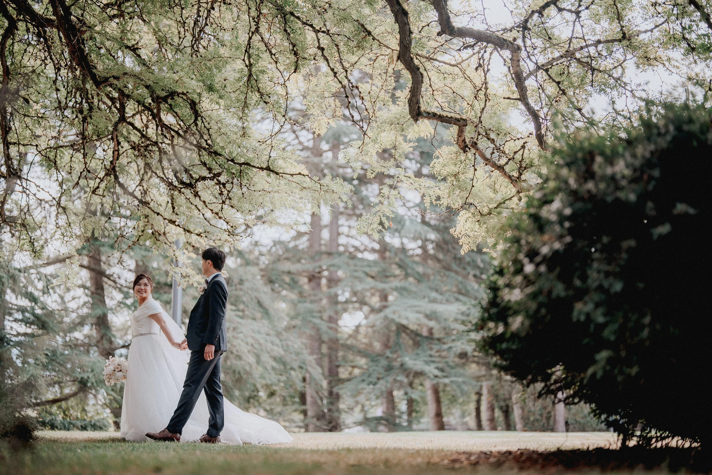 Couple walking hand in hand along a sunlit garden path.