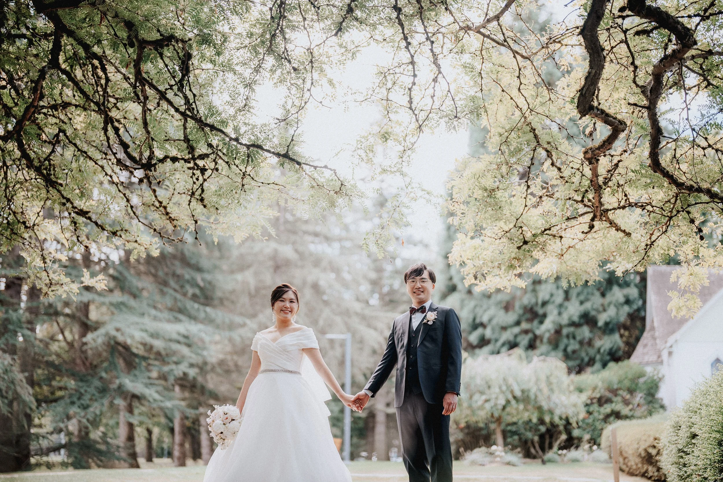Bride and groom holding hands in the tree-lined chapel gardens.