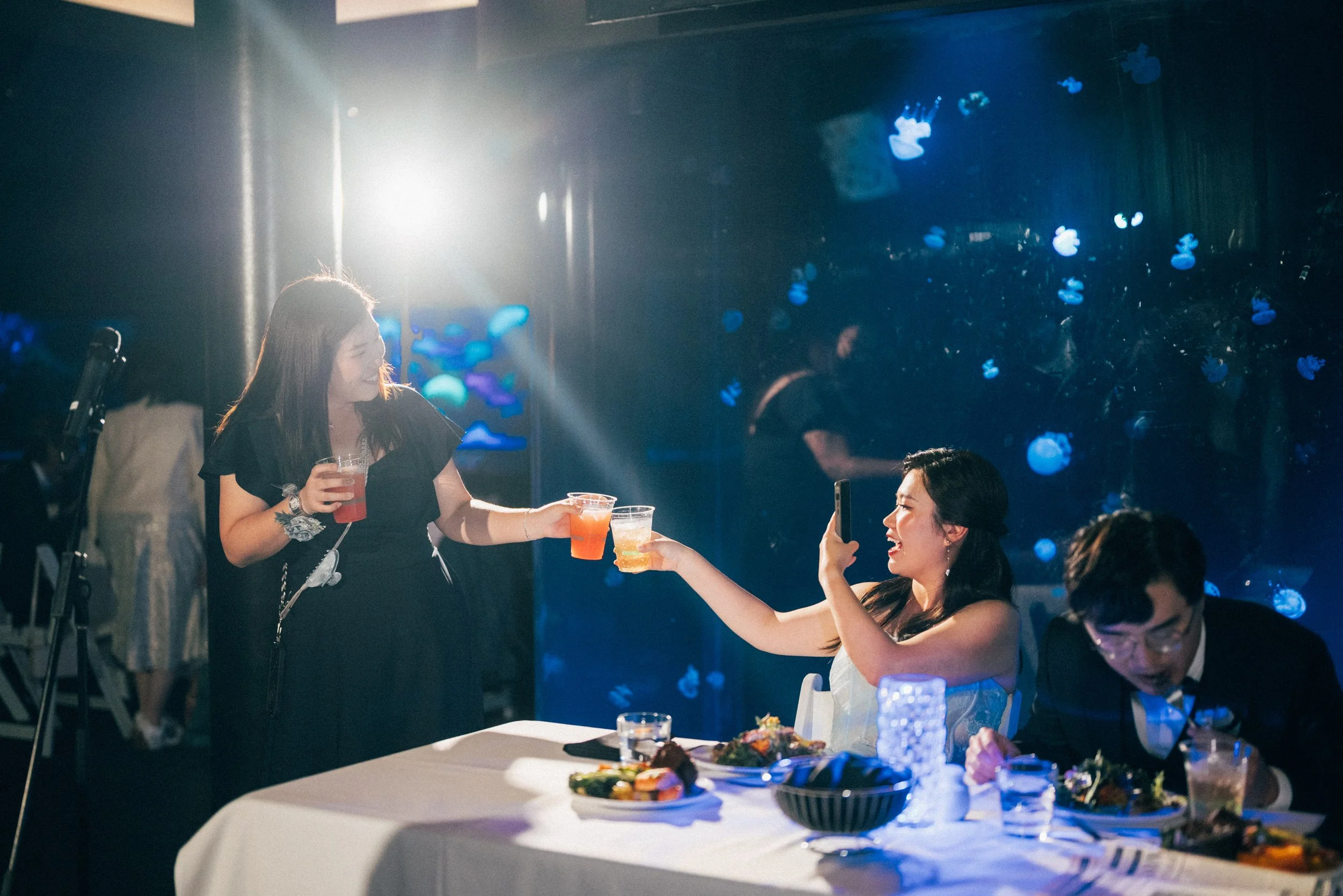 Bride sharing a toast with guests beside the blue-lit aquarium tank.