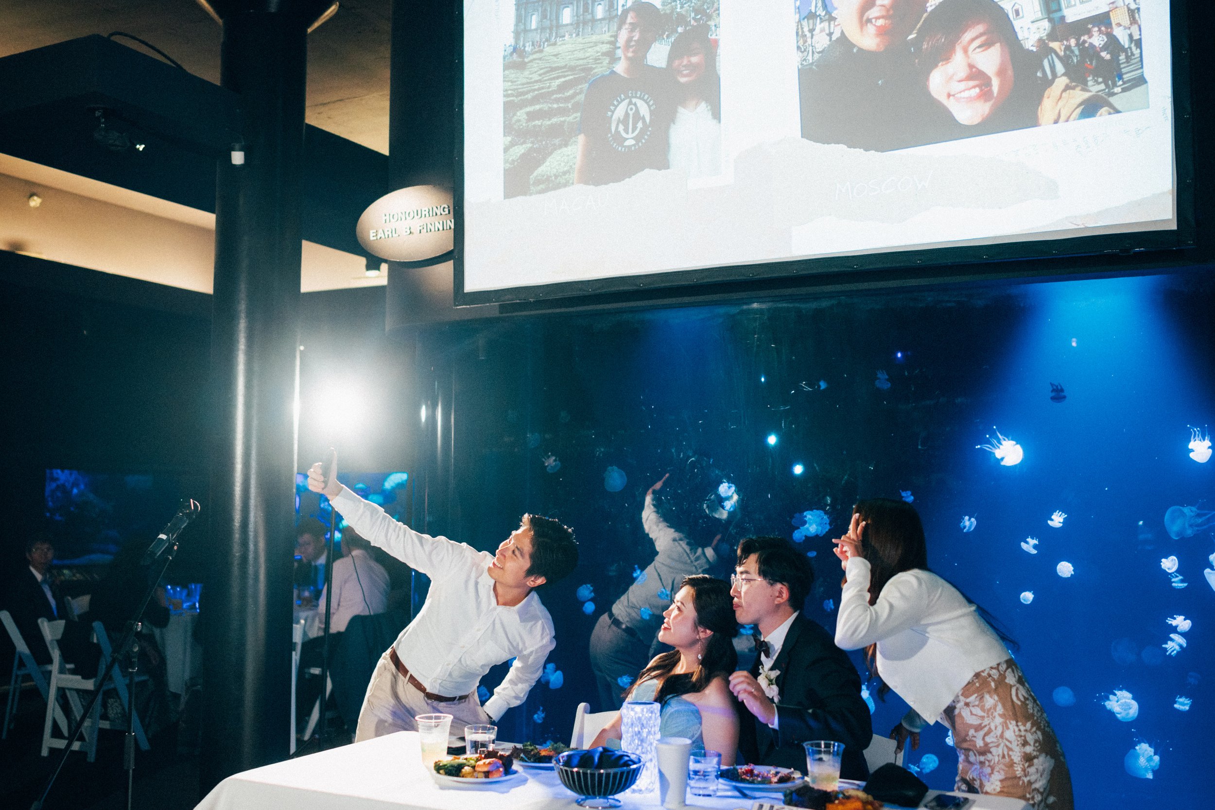 Wedding guests taking a group selfie beneath the reception slideshow.