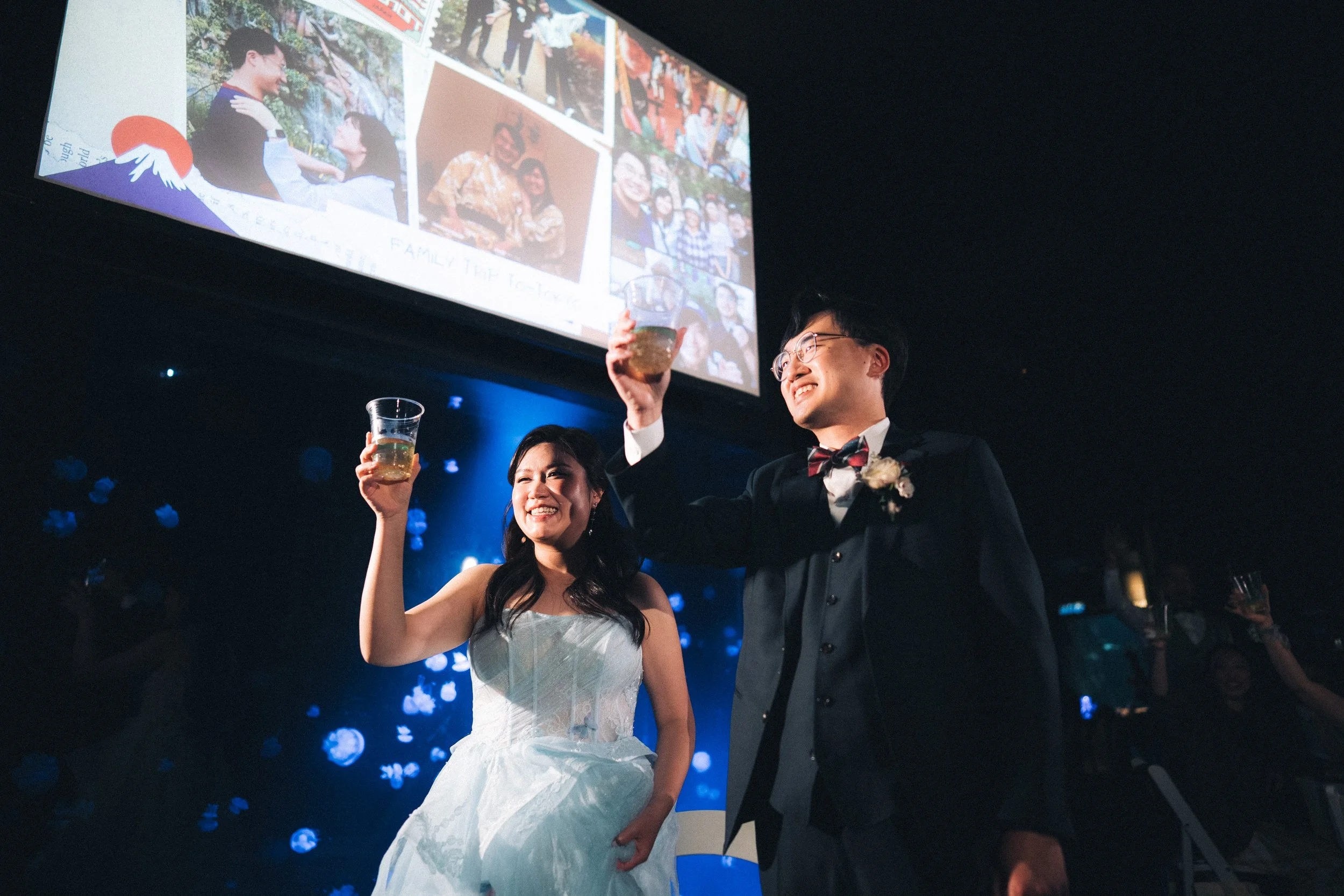 Bride and groom raising their glasses beneath a projected photo slideshow.