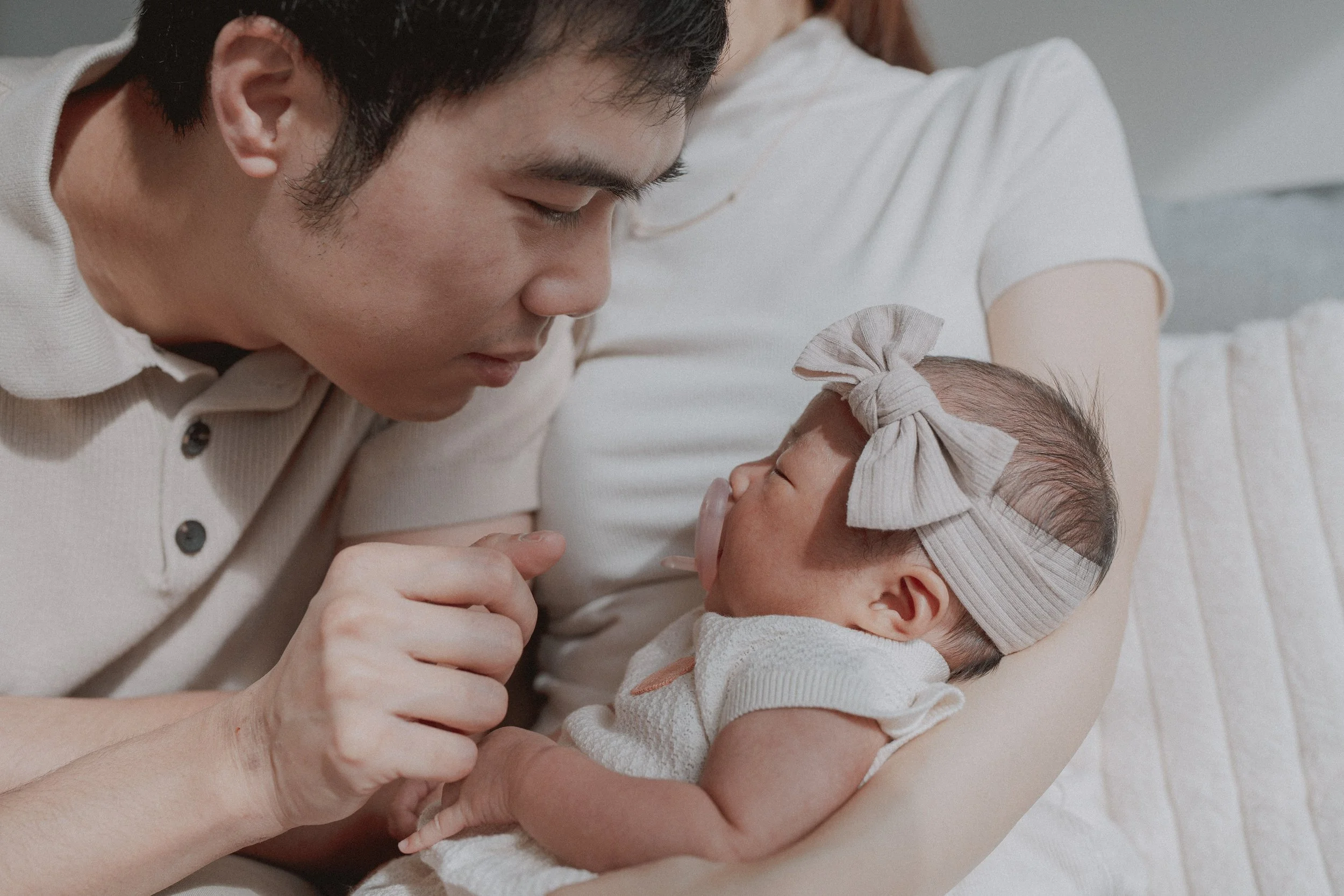 Parent leaning toward a newborn resting in another parent's arms.