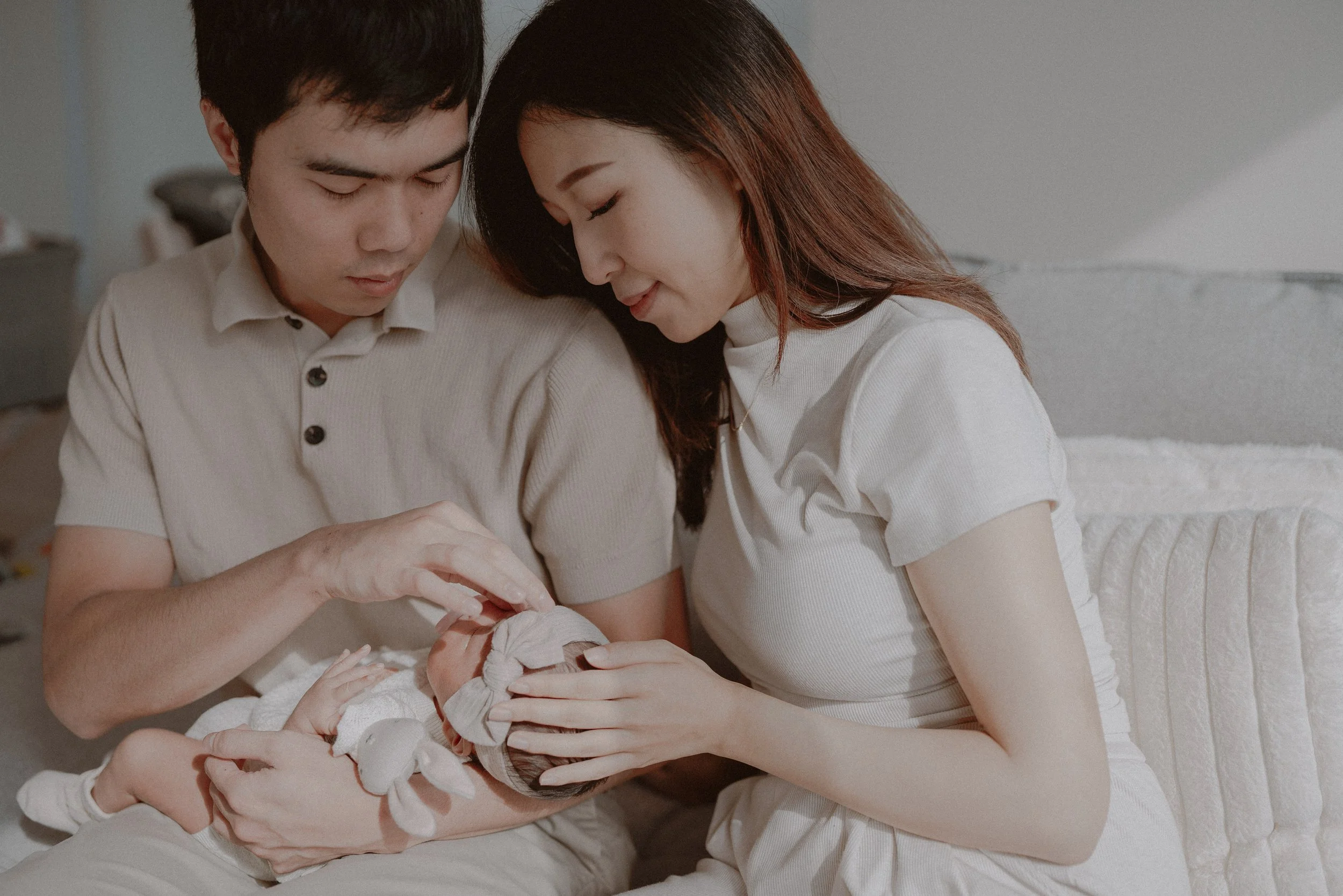 Parents gently holding their baby together in warm window light.