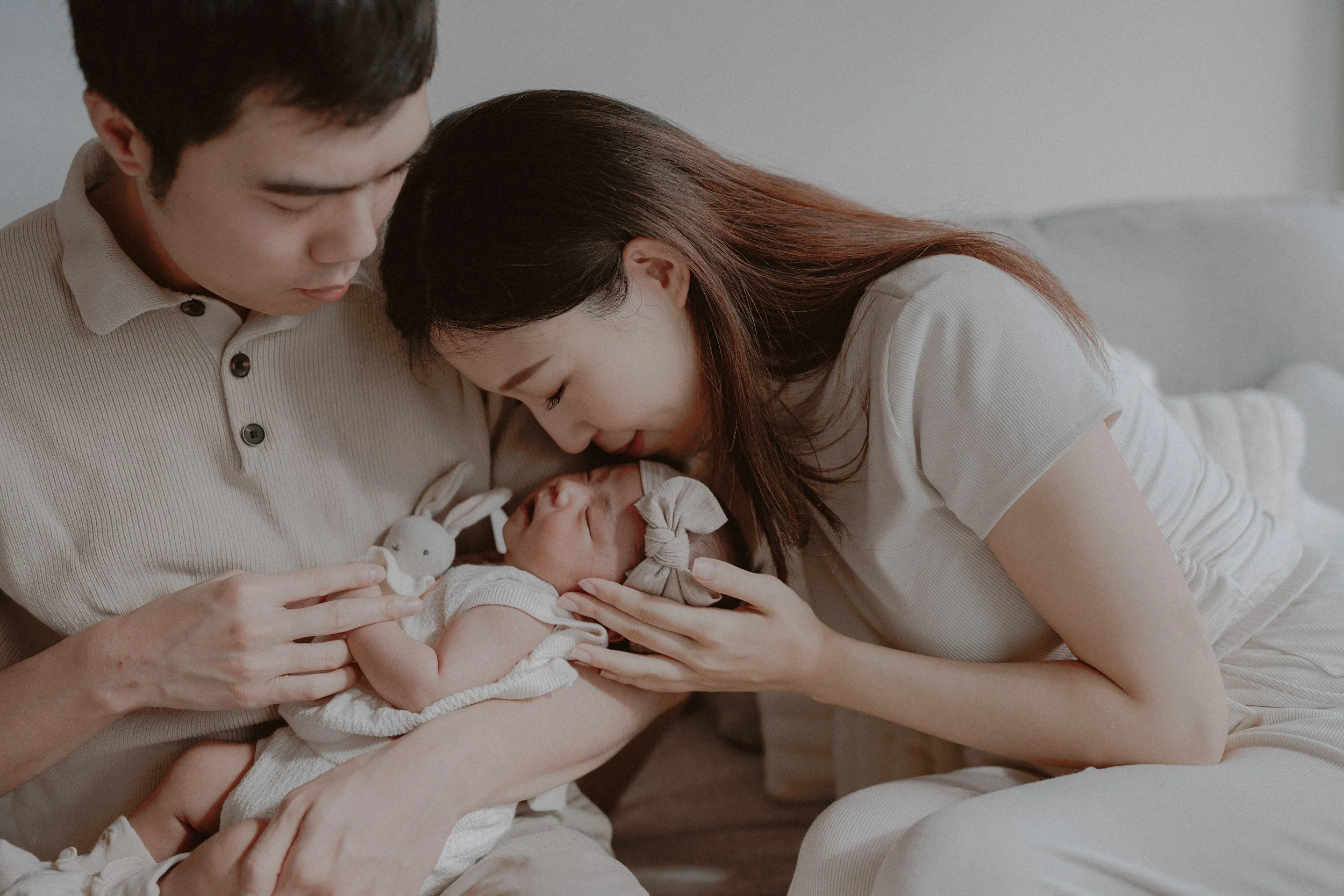 Parents leaning close to their newborn on a pale sofa.