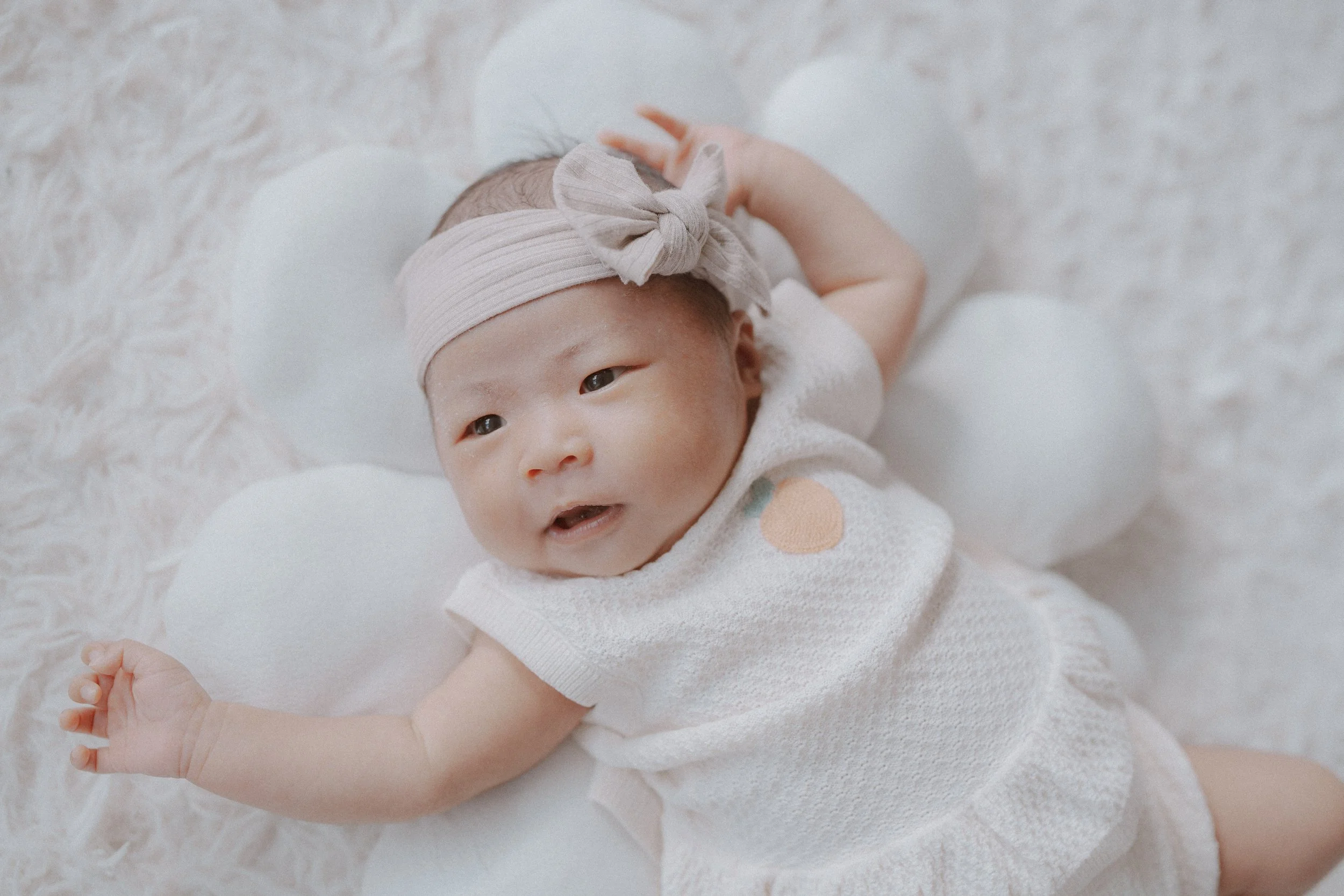 Awake newborn with a bow headband looking toward the camera.