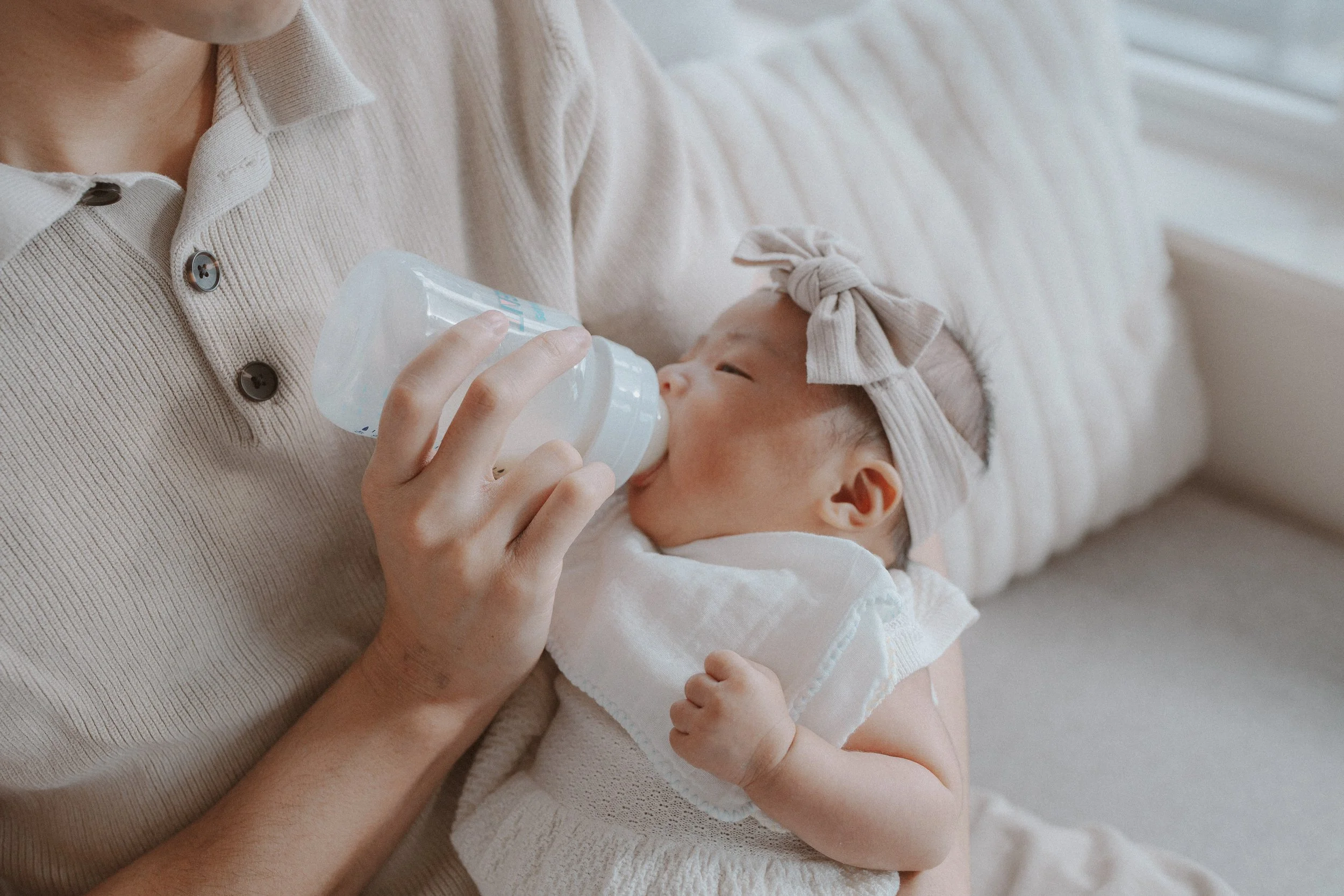 Parent bottle-feeding a newborn resting in their lap.