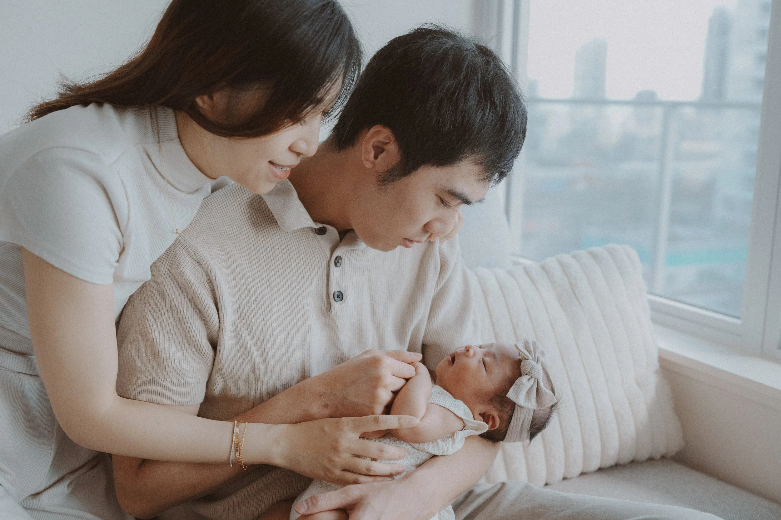 Parents leaning together over their newborn on a sofa.