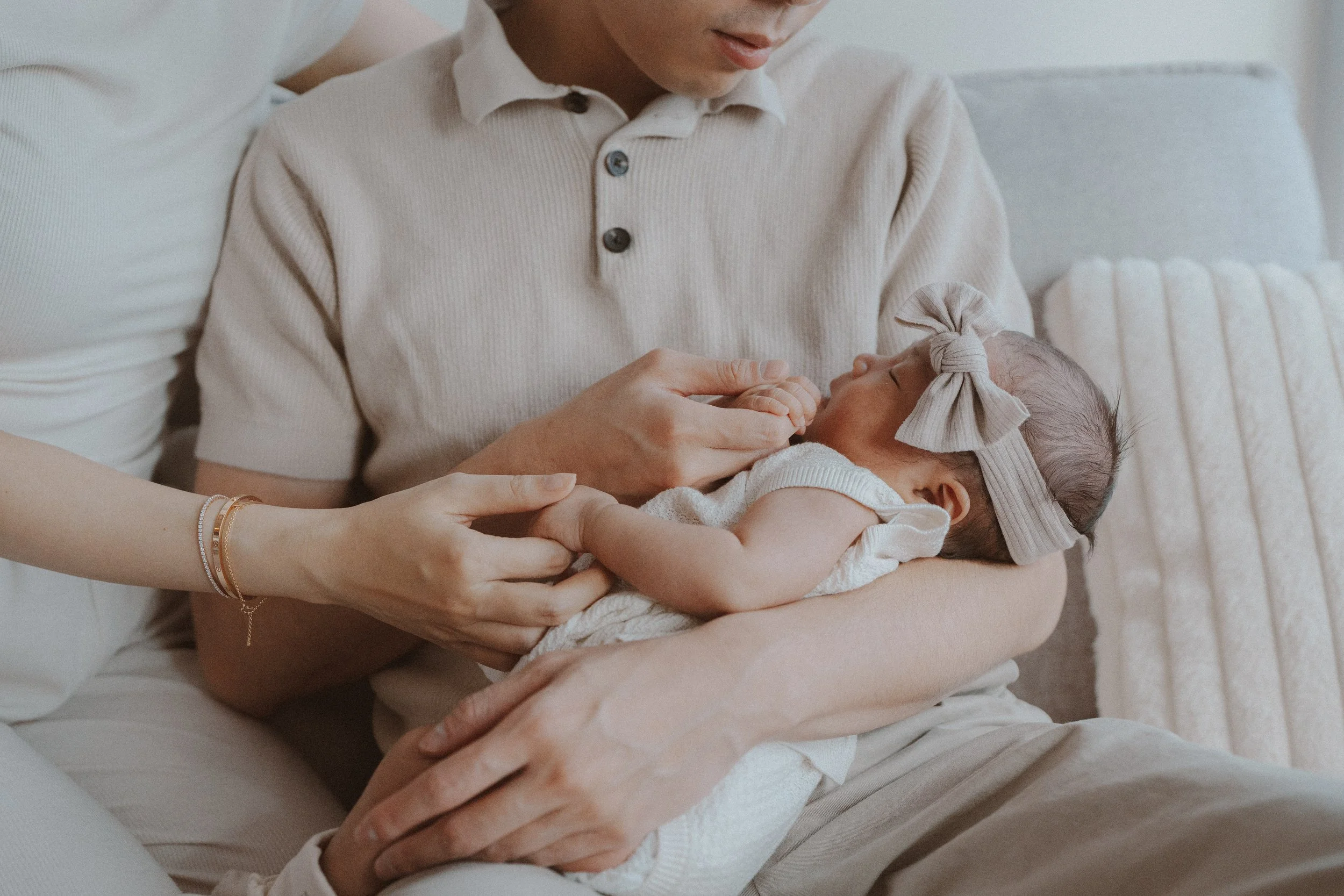 Parents gently touching their newborn resting across a lap.