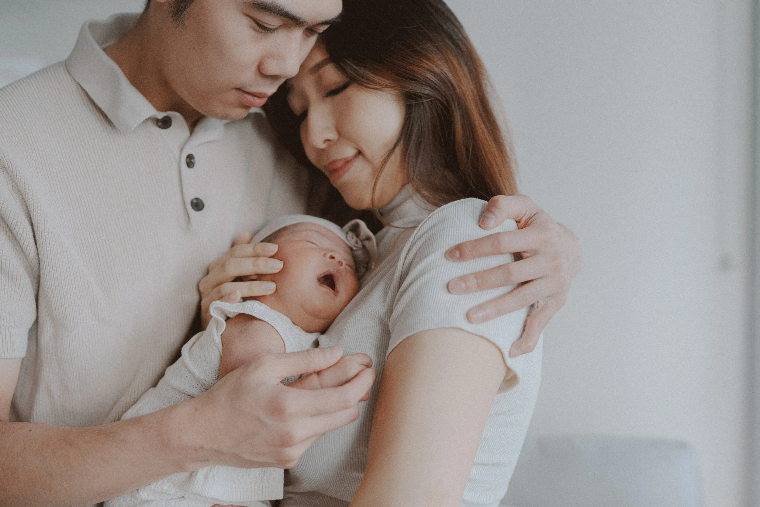 Parents embracing with their newborn held between them.