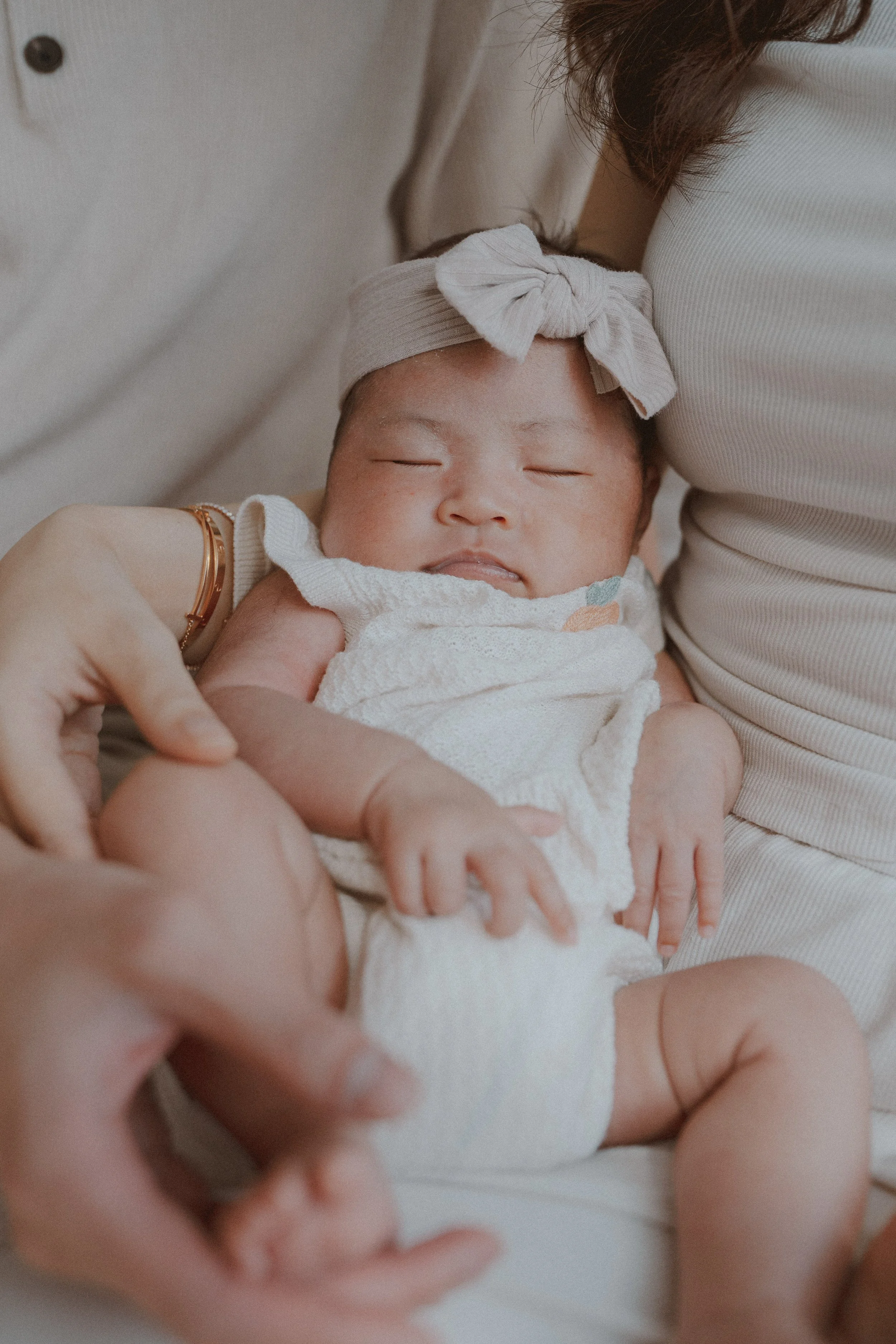 Newborn with a bow headband nestled against a parent on a sofa.