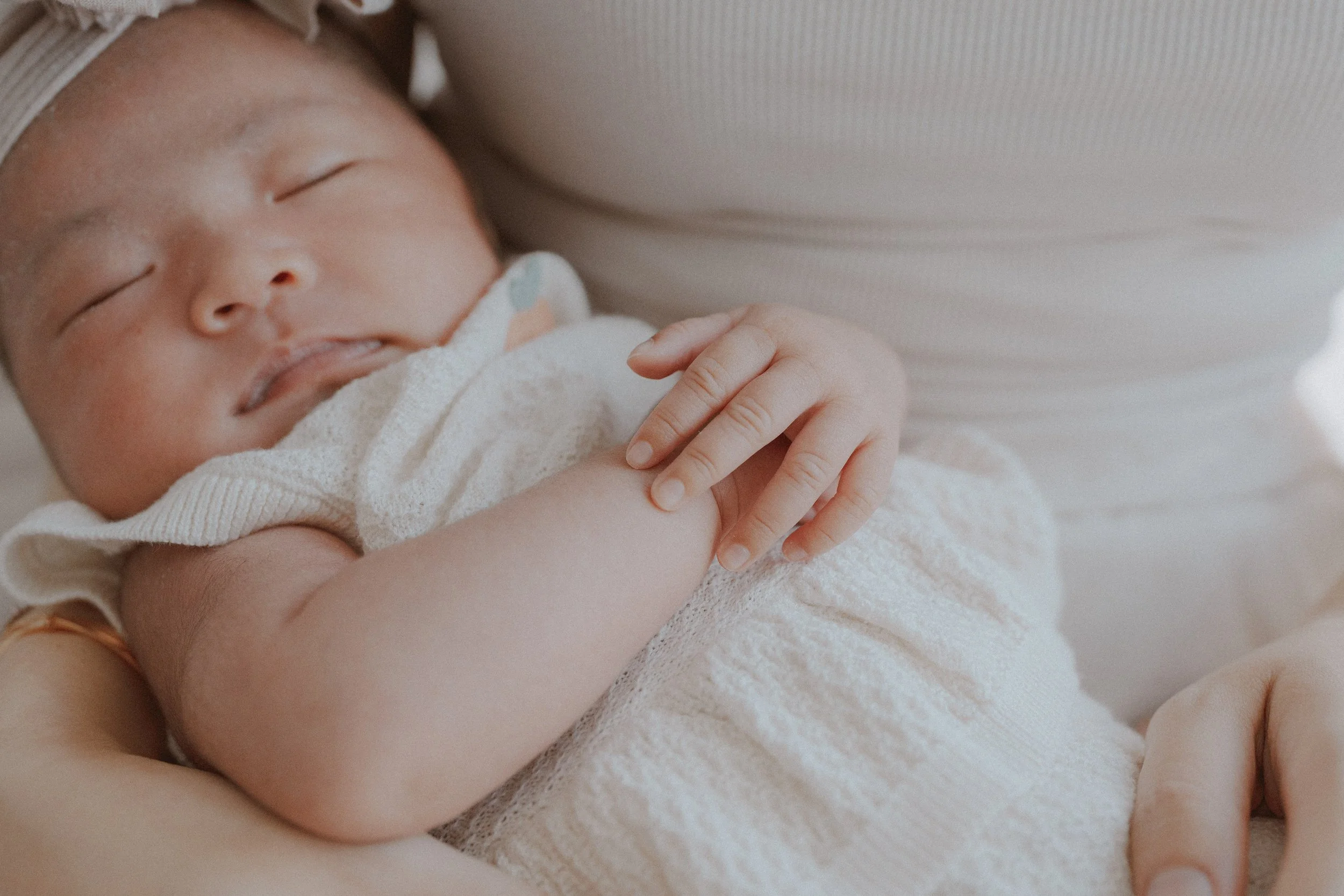Sleeping newborn's face and folded hand resting against a parent's chest.