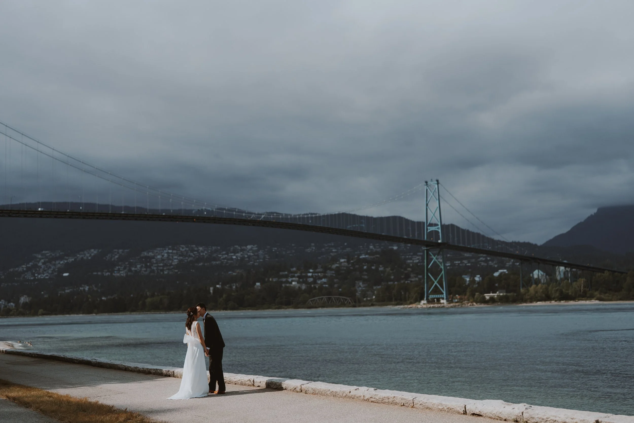 Wide Stanley Park waterfront engagement scene beneath Lions Gate Bridge
